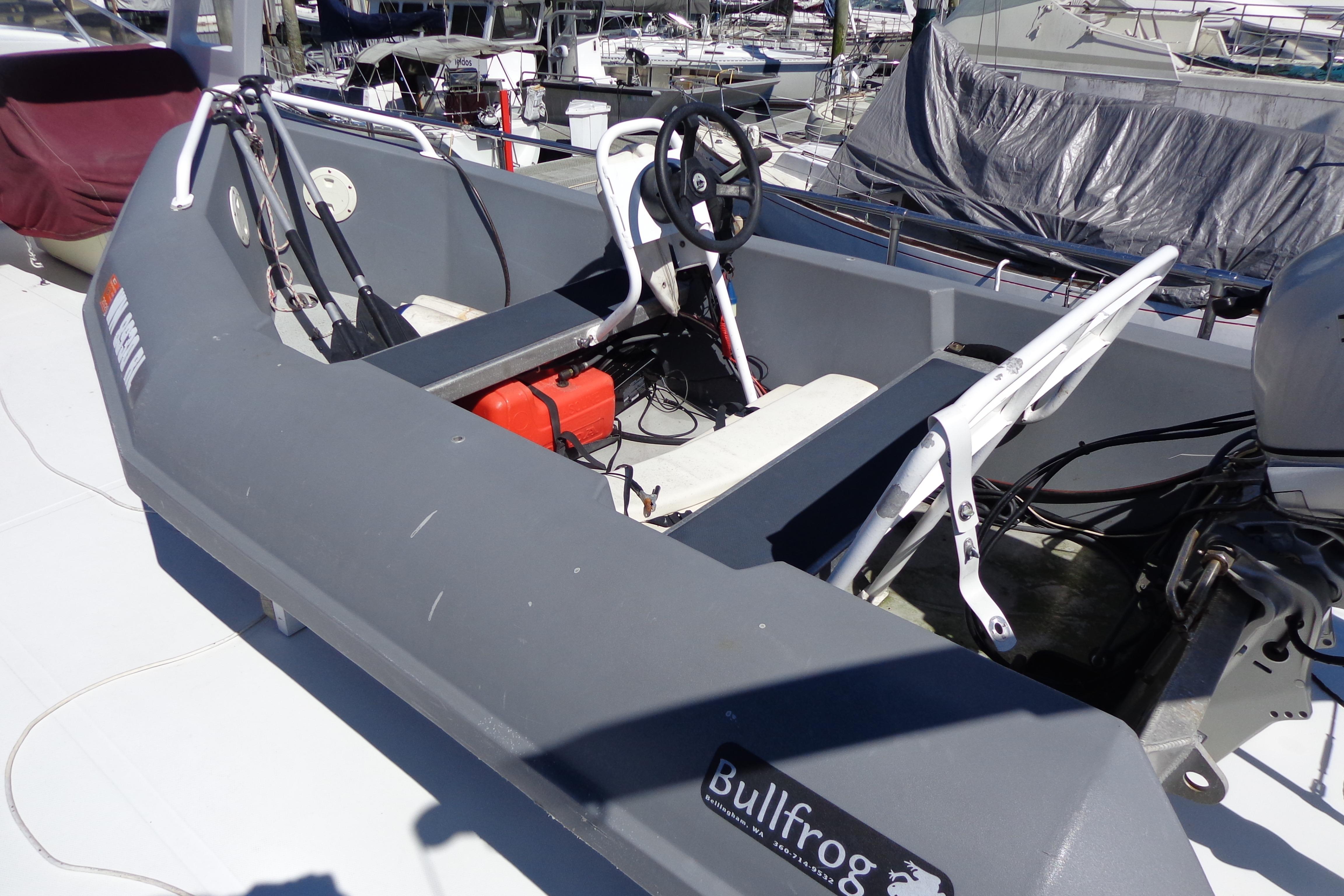 Small boat with steering wheel and seats, docked near other vessels, labeled "Bullfrog."