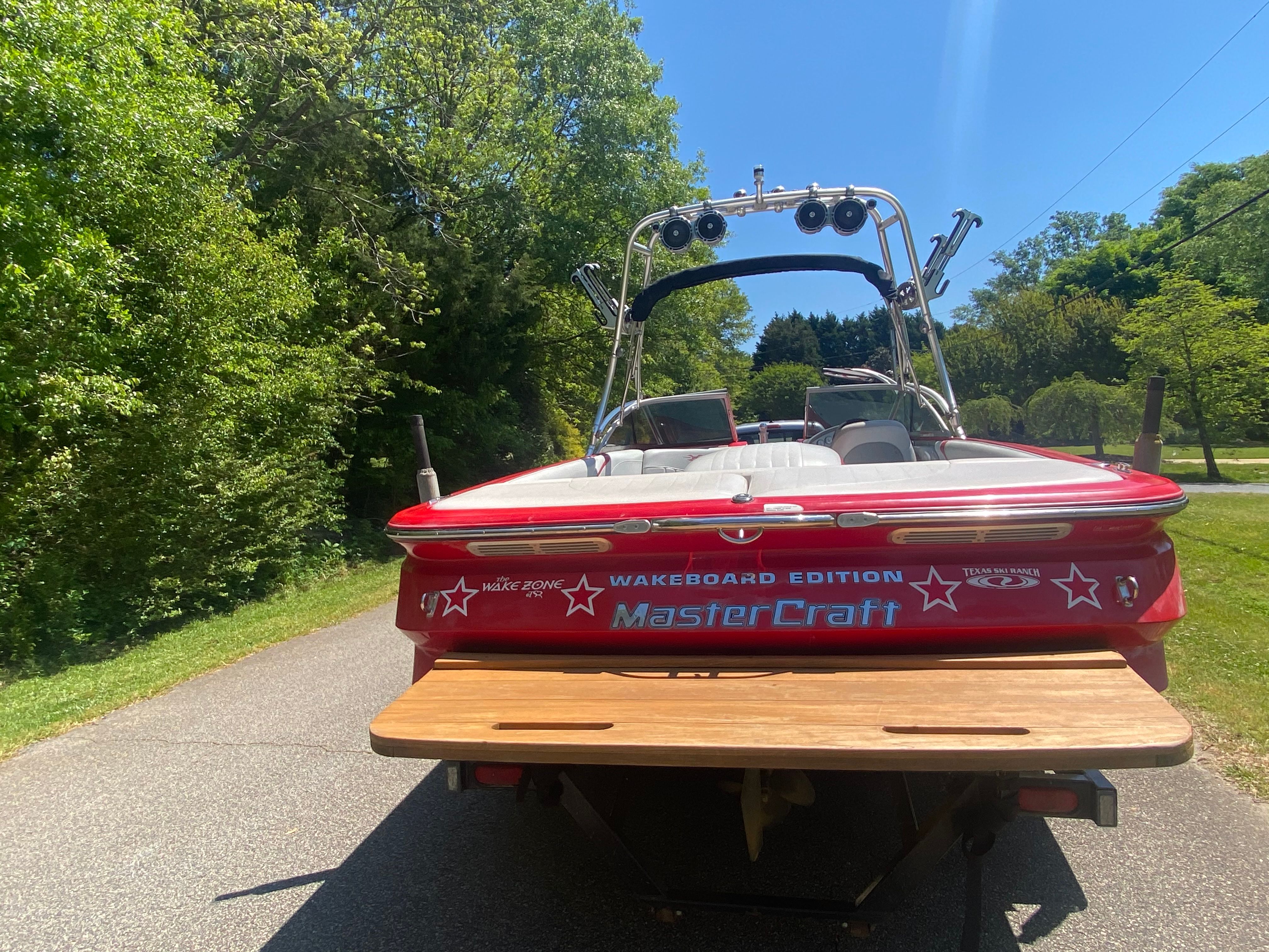 Red 2004 MasterCraft X-9 boat on a trailer, surrounded by trees.