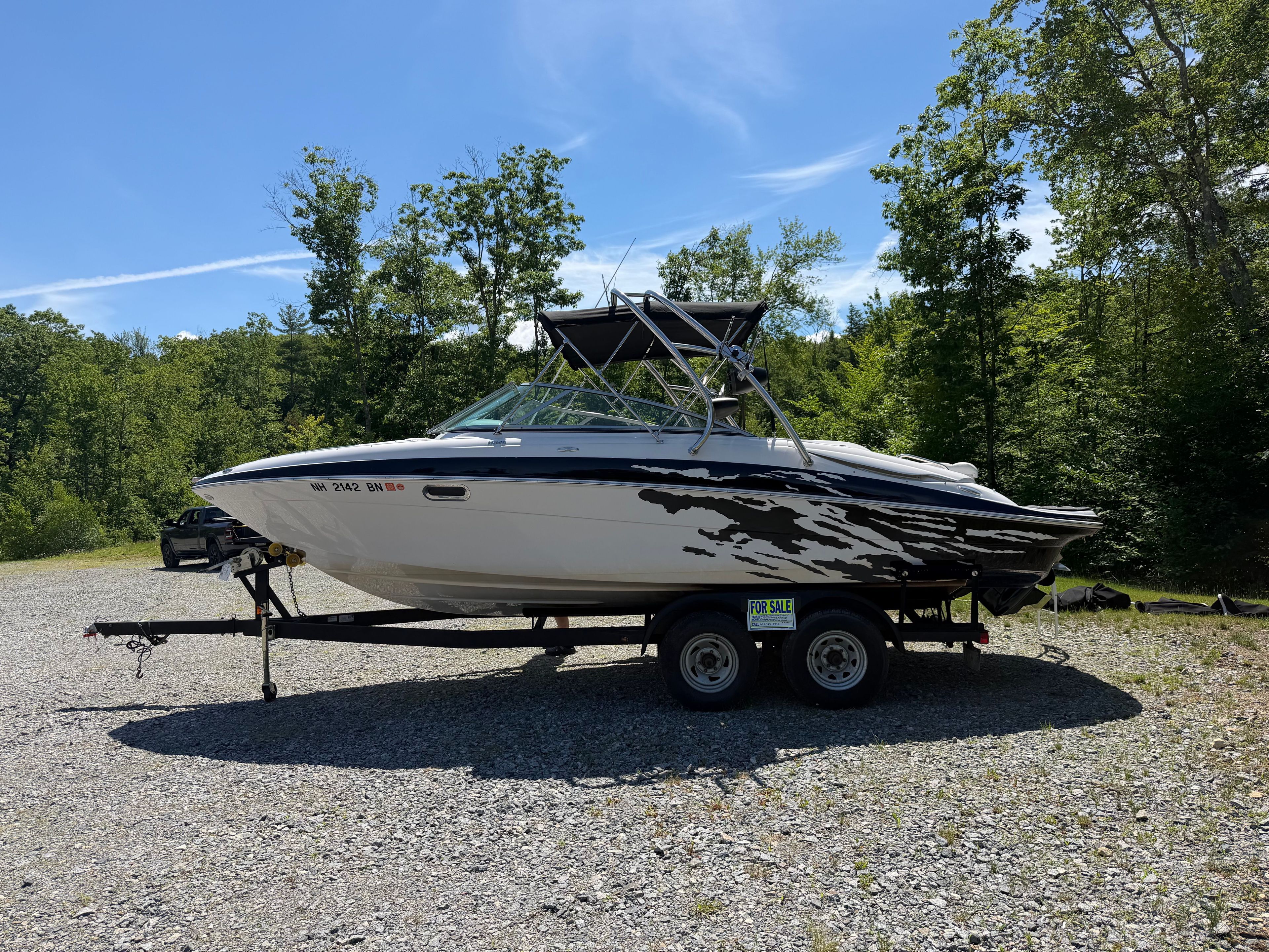 A 2008 Four Winns H240 Frenzy boat on a trailer, surrounded by trees and blue sky.