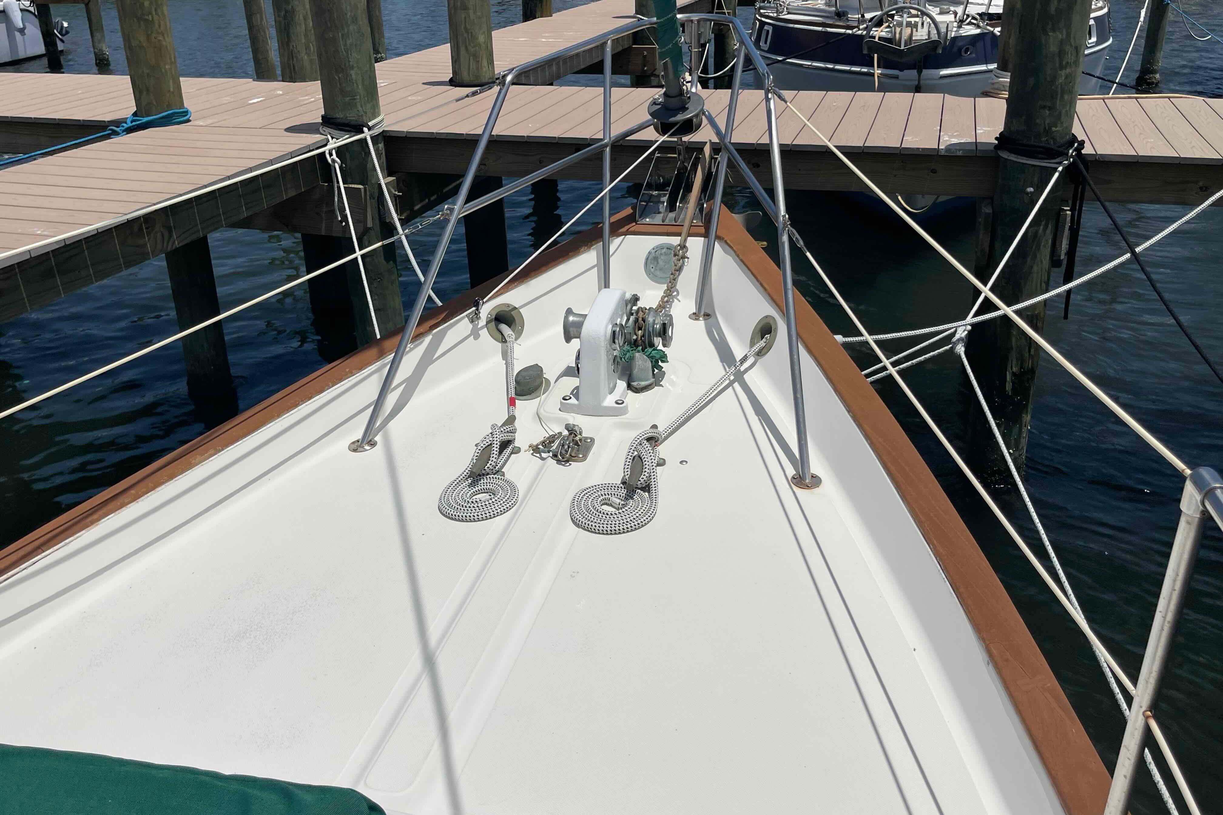 Bow of 1987 Pacific Seacraft 34 sailboat docked at marina, featuring anchor and ropes.