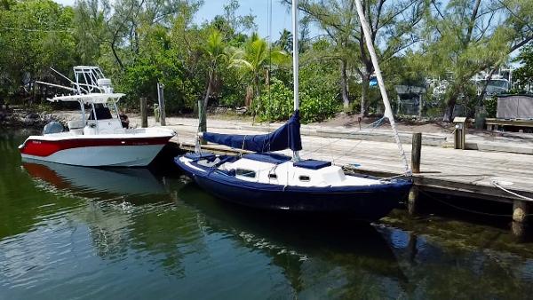 1968 Sailboat 24 docked beside a motorboat, surrounded by lush greenery.
