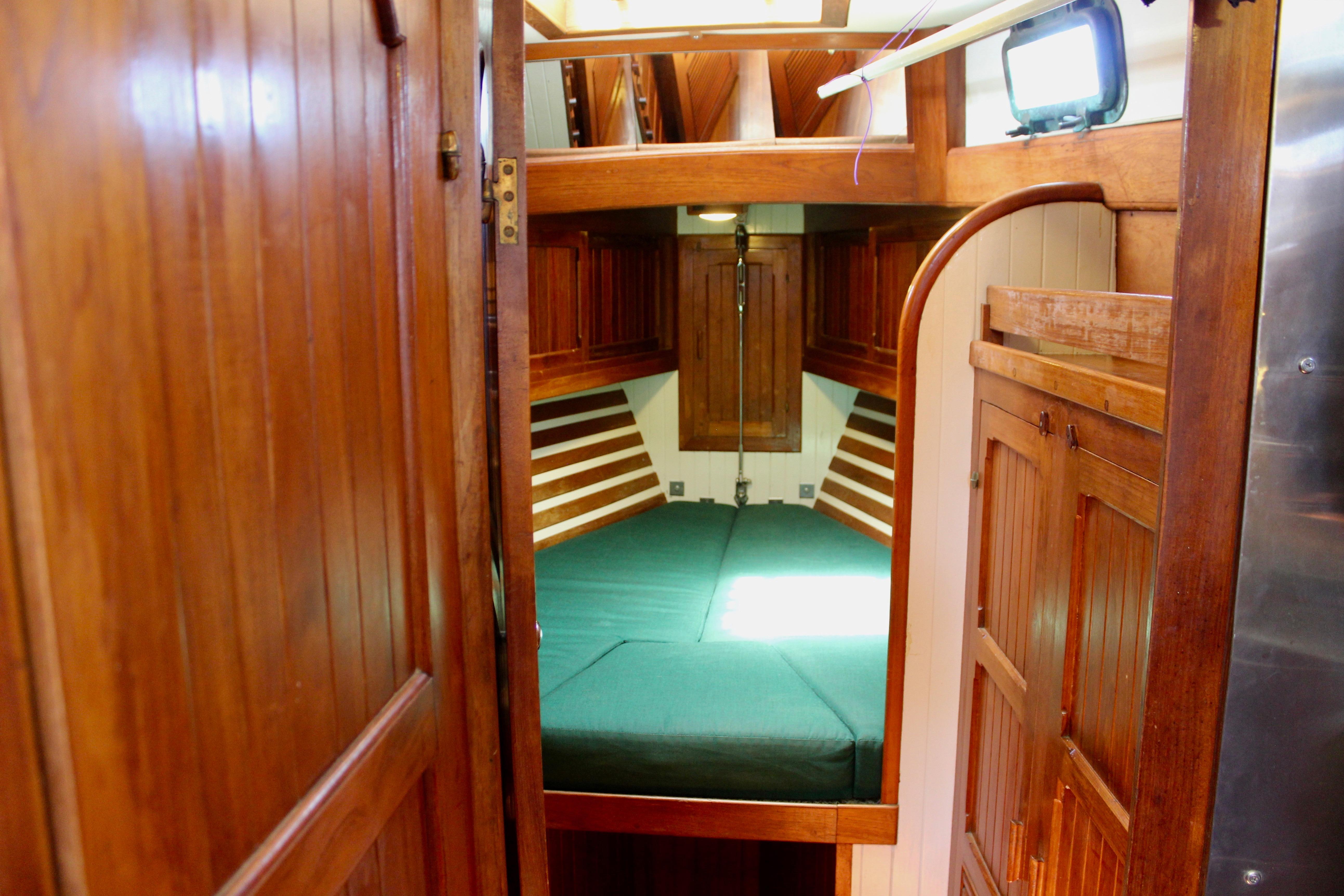 Interior cabin of 1981 Kelly Peterson 46 sailboat with wooden furnishings and green bedding.