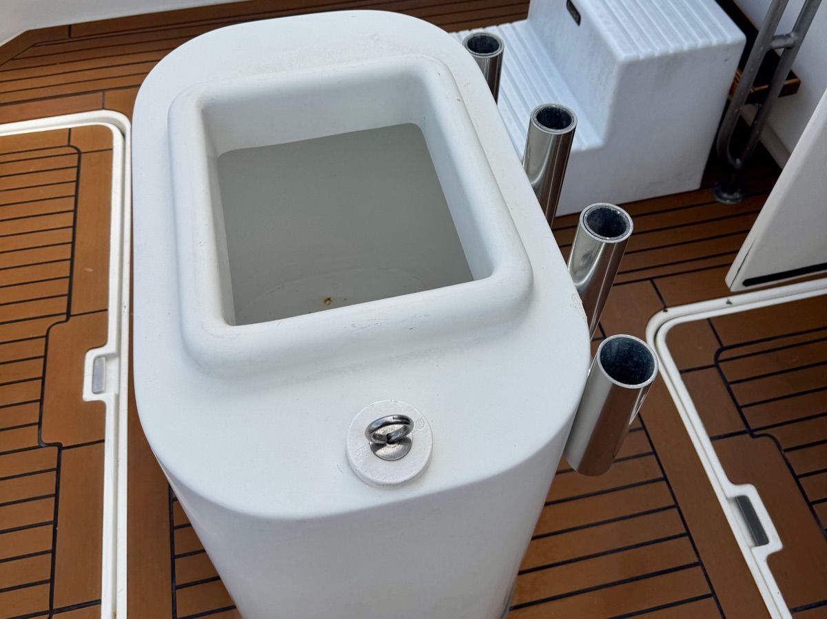 A fishing boat with a white fish container and rod holders on a wooden deck.