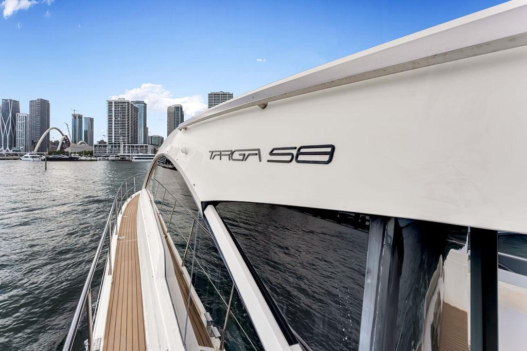 2012 Fairline Targa 58 yacht cruising near city skyline, clear blue sky.