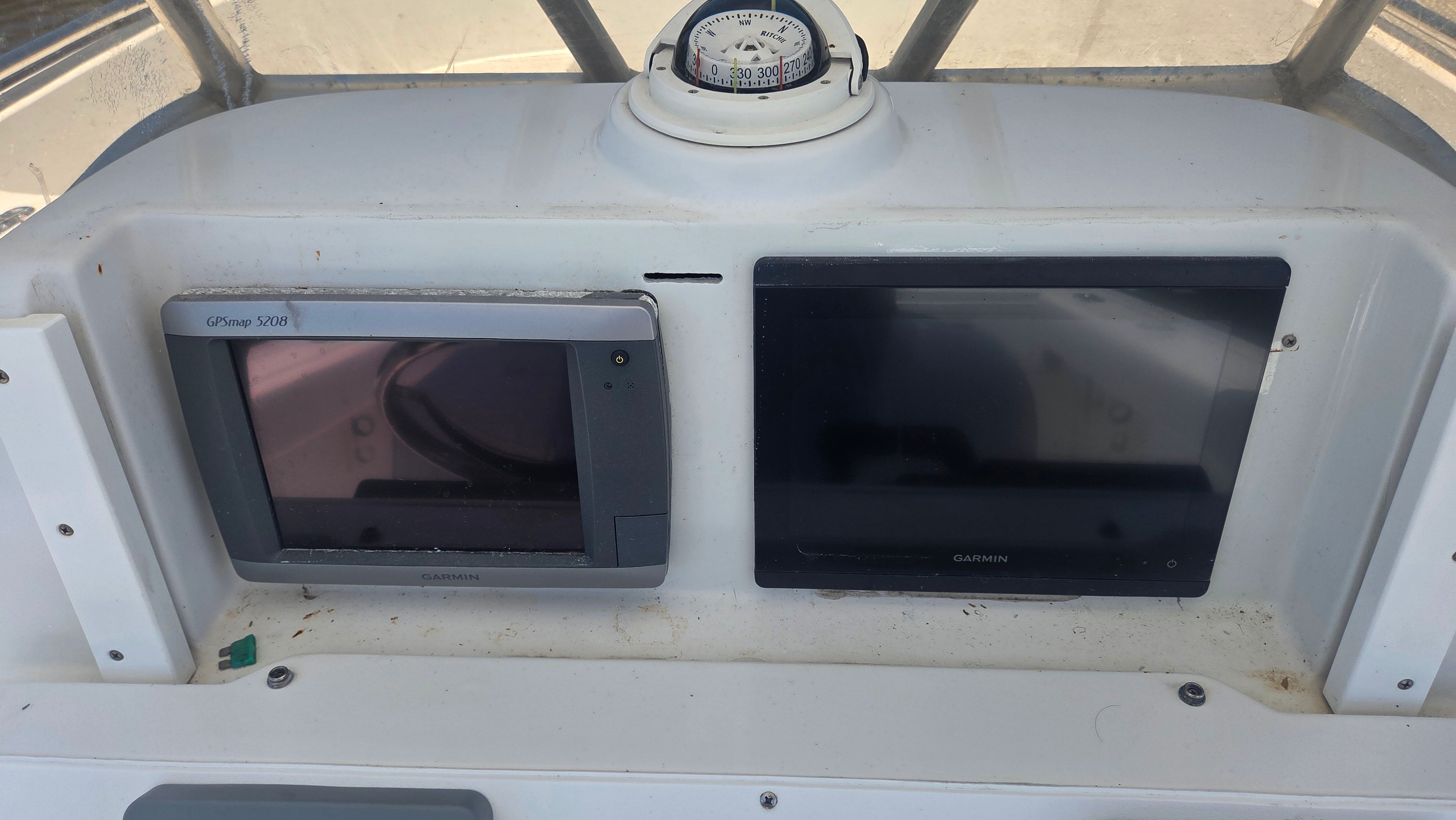 Two Garmin screens and a compass on a boat's dashboard.
