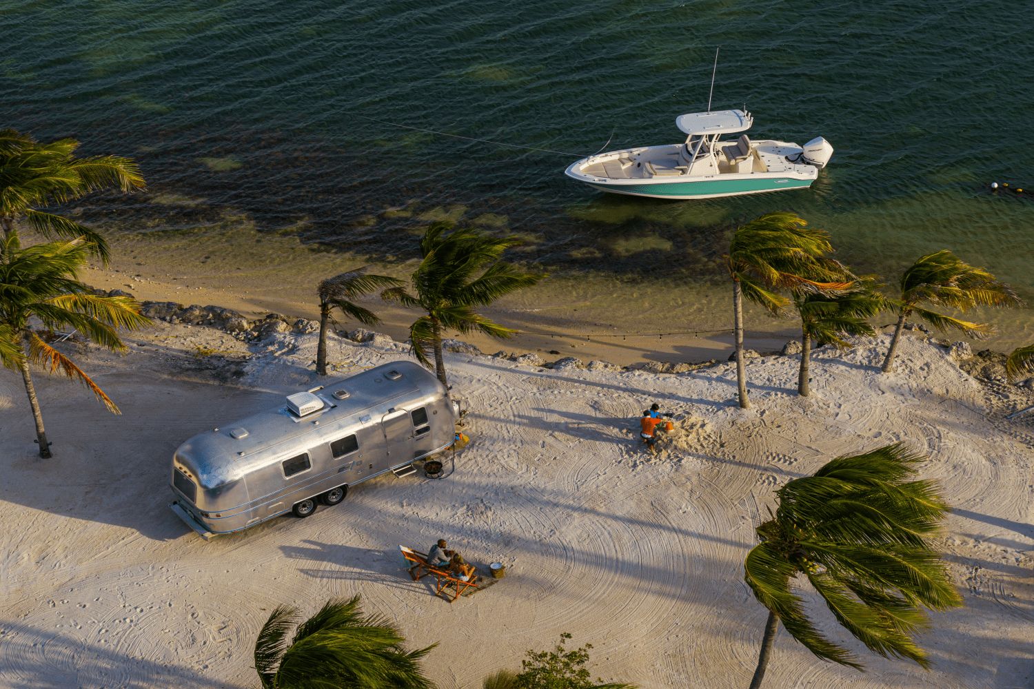 A Boston Whaler 25DA boat is anchored in clear water near a sandy shore with palm trees.