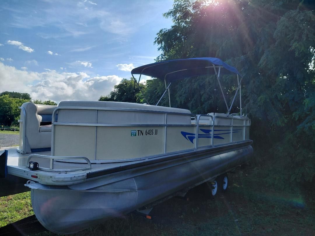 1999 Premier 250 Grand Majestic pontoon boat with blue canopy, on a trailer outdoors.