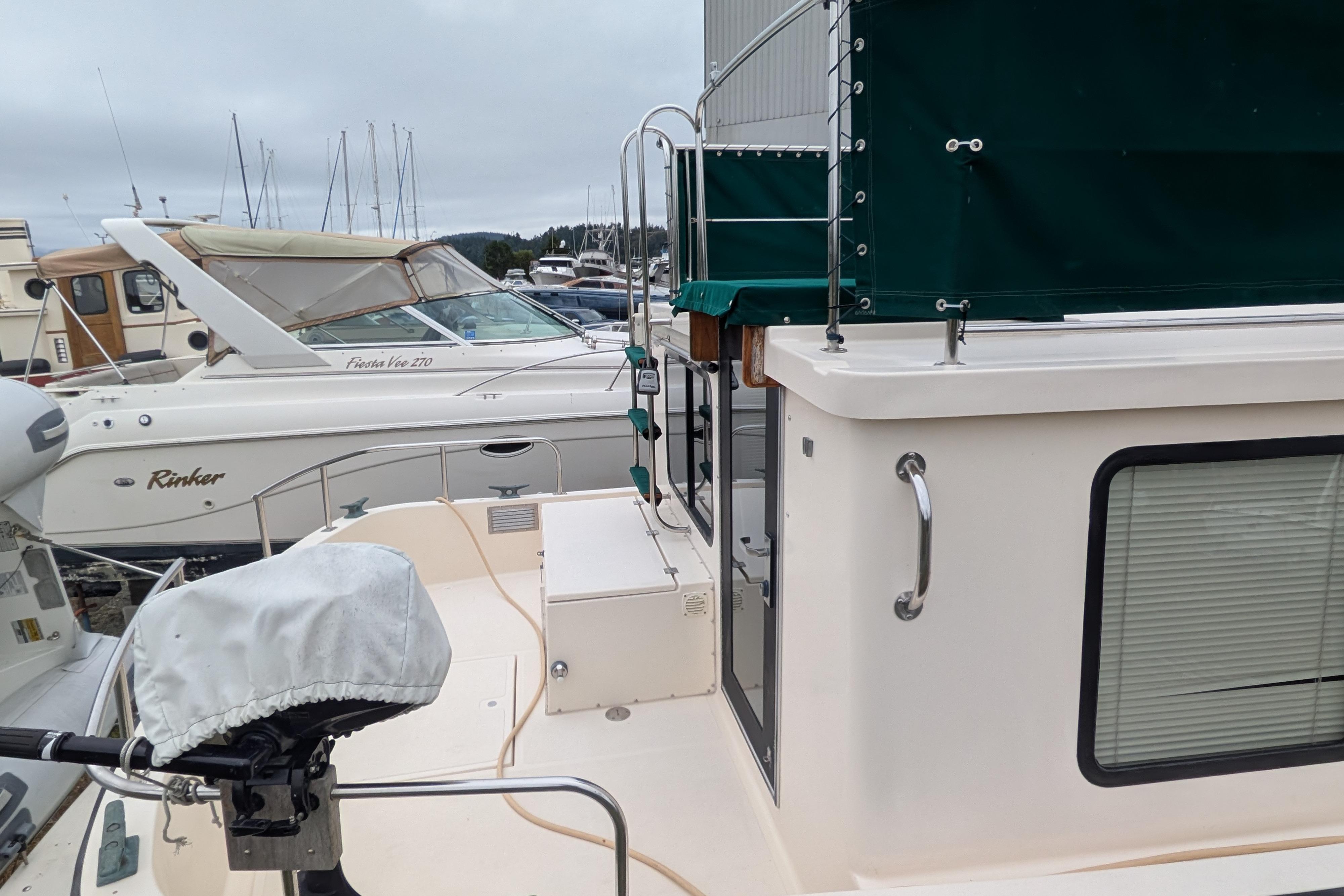 1998 Nordic Tug 32 docked, featuring green canopy and adjacent boats in marina.