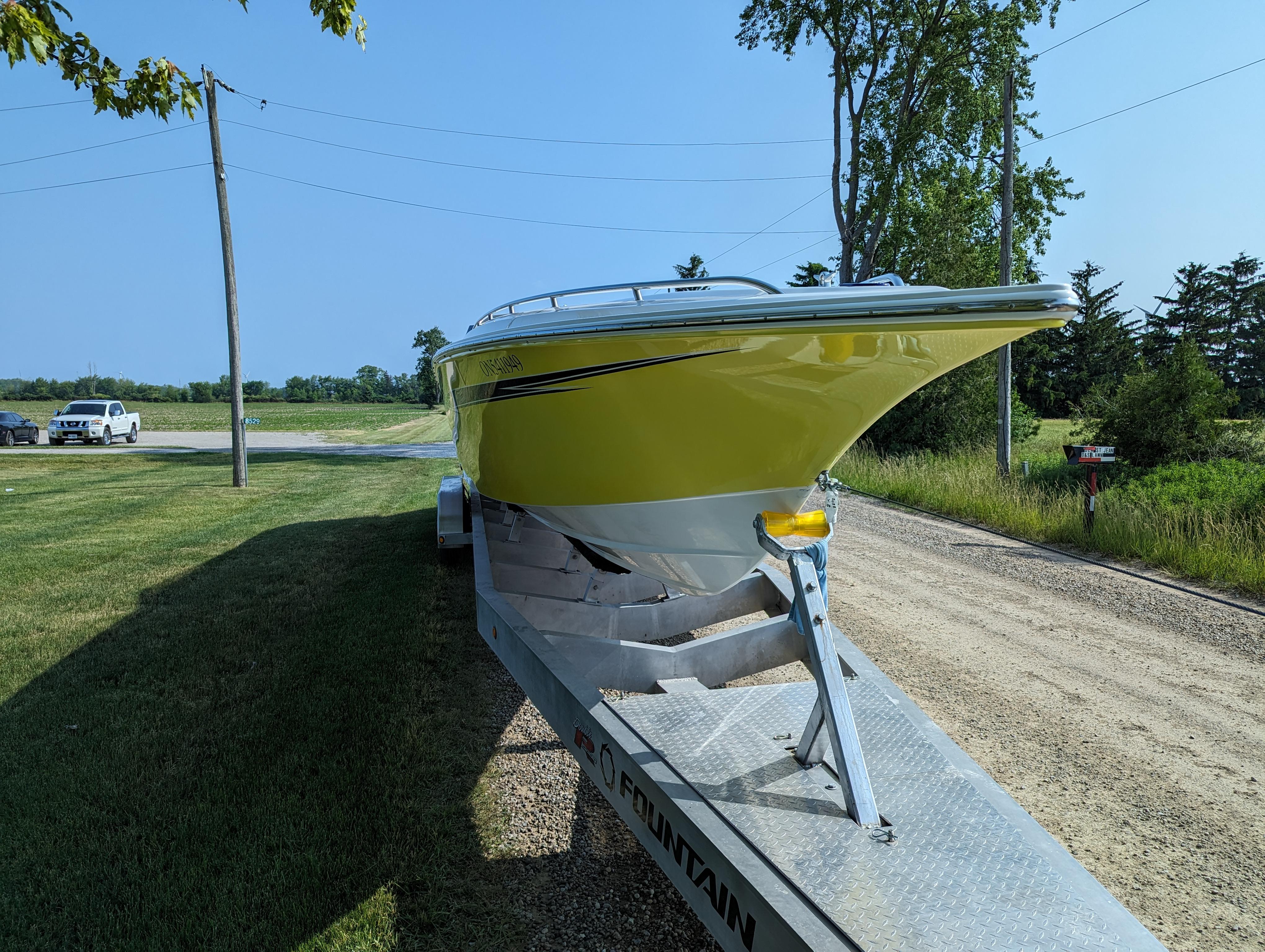 2006 Fountain 42 boat on trailer, parked on a rural road with trees and grass.
