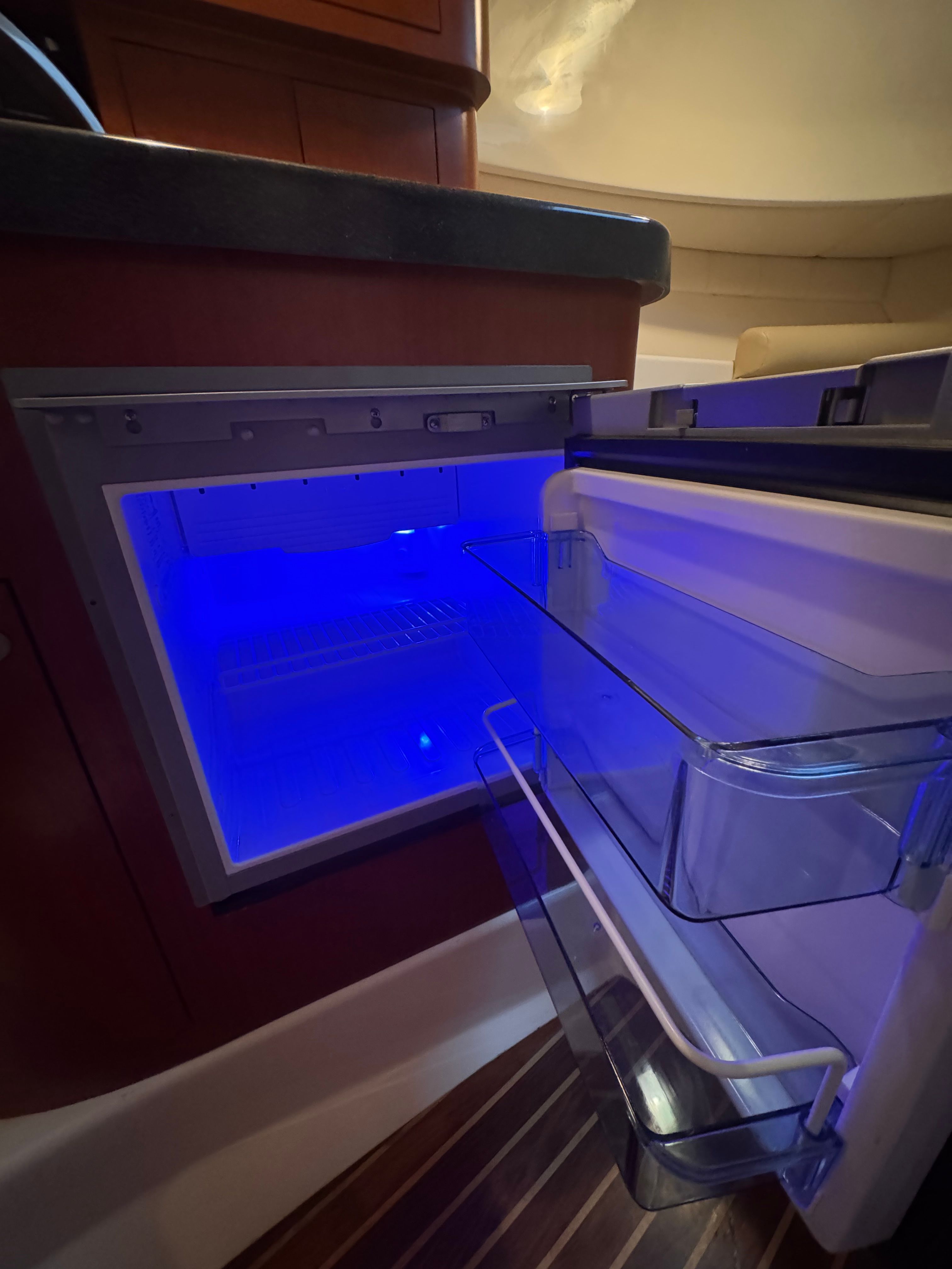 An open refrigerator with blue lighting inside, built into a boat's galley.
