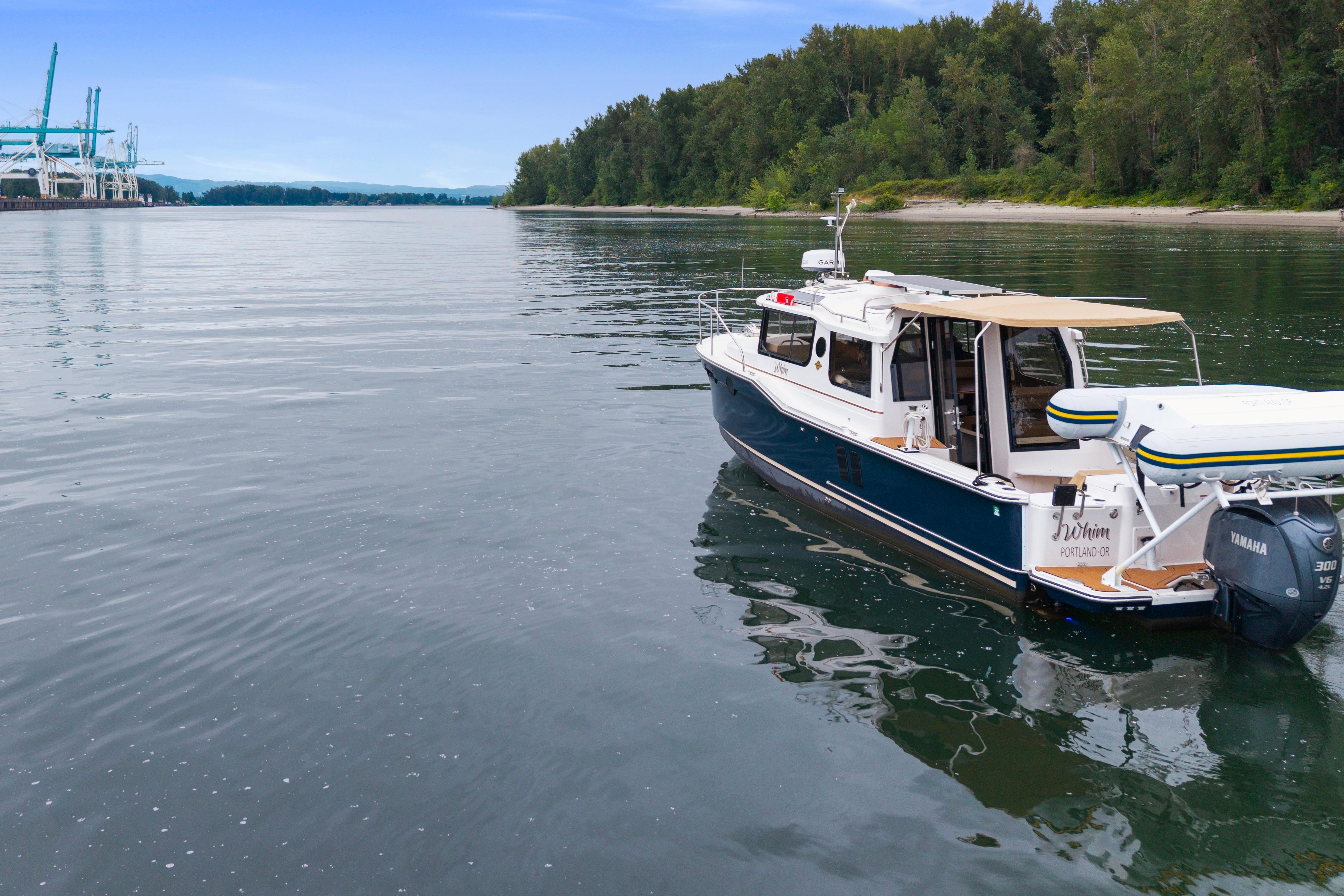 2022 Ranger Tugs R-27 boat on calm water near a forested shoreline.