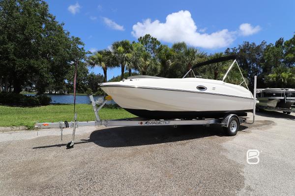 2018 Bayliner 210 DB boat on trailer, parked near a scenic lake with palm trees.