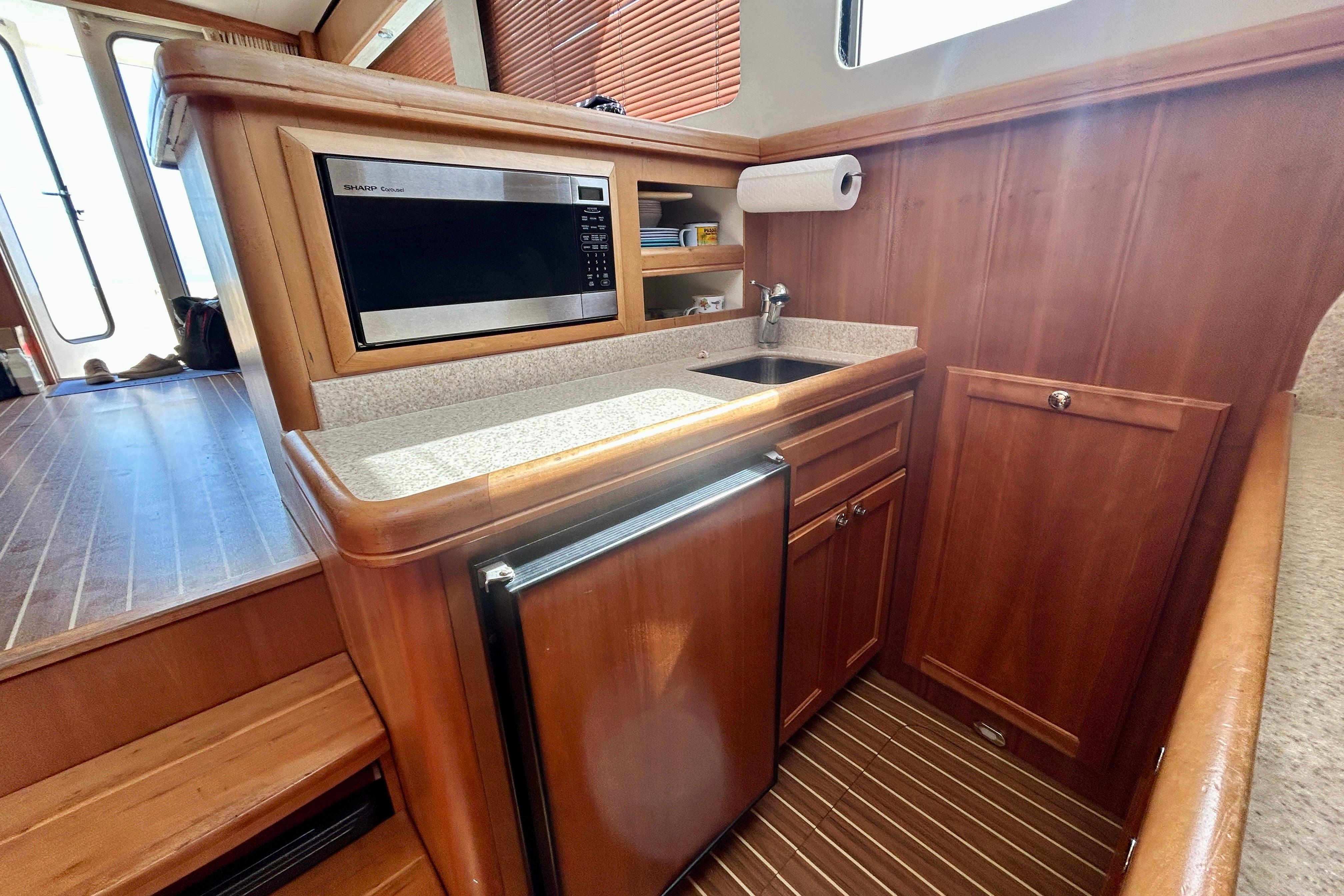 2006 Mainship 34 Trawler kitchen with wood cabinetry, microwave, sink, and compact refrigerator.