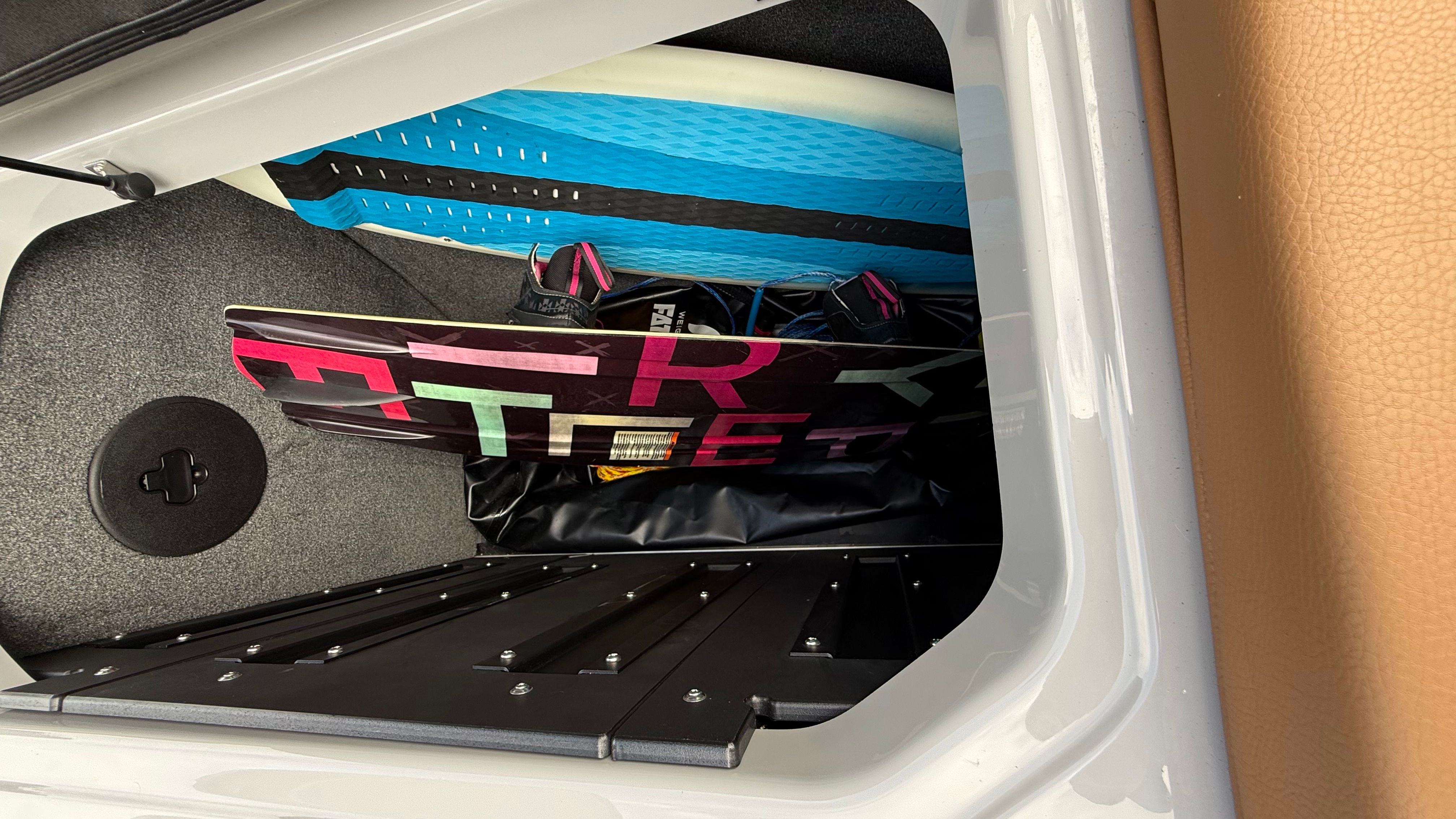 A storage compartment with a wakeboard and a blue mat.