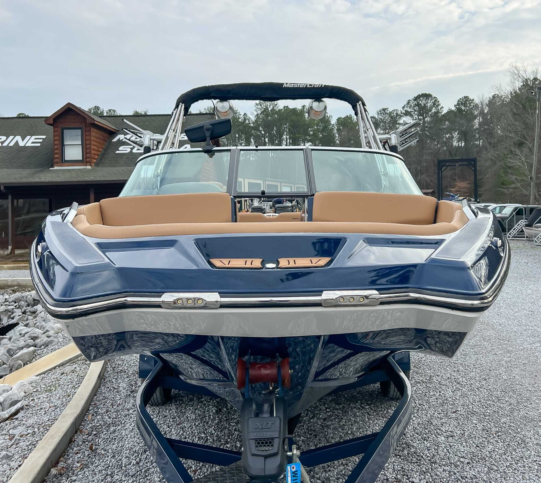 2021 MasterCraft XT22 boat, blue, on gravel path in front of log cabin.
