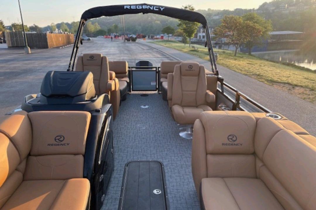 2026 Regency 230 DL pontoon boat with tan seating, parked near a scenic waterfront.