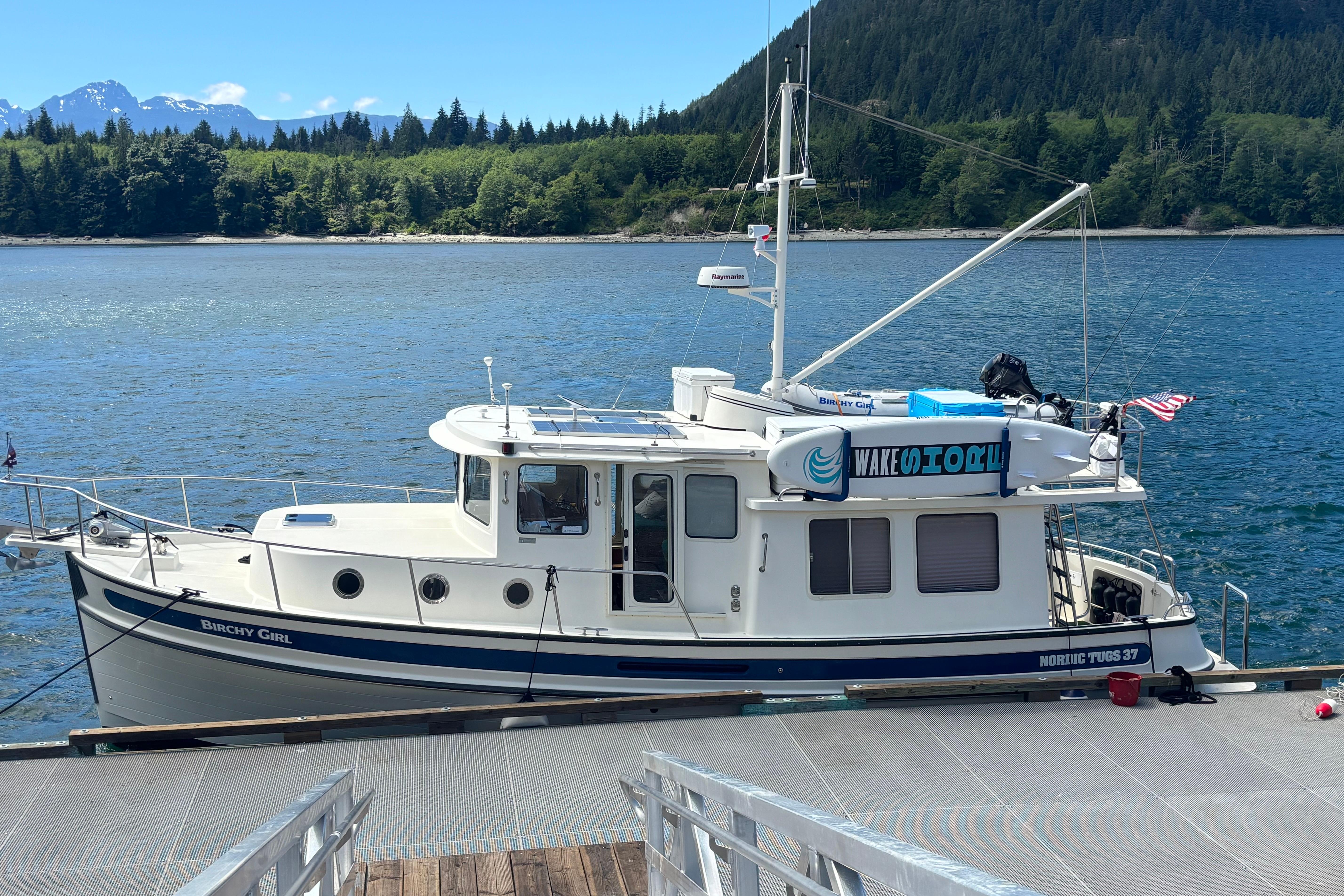 2004 Nordic Tug 37 docked by scenic forested shoreline and mountains.