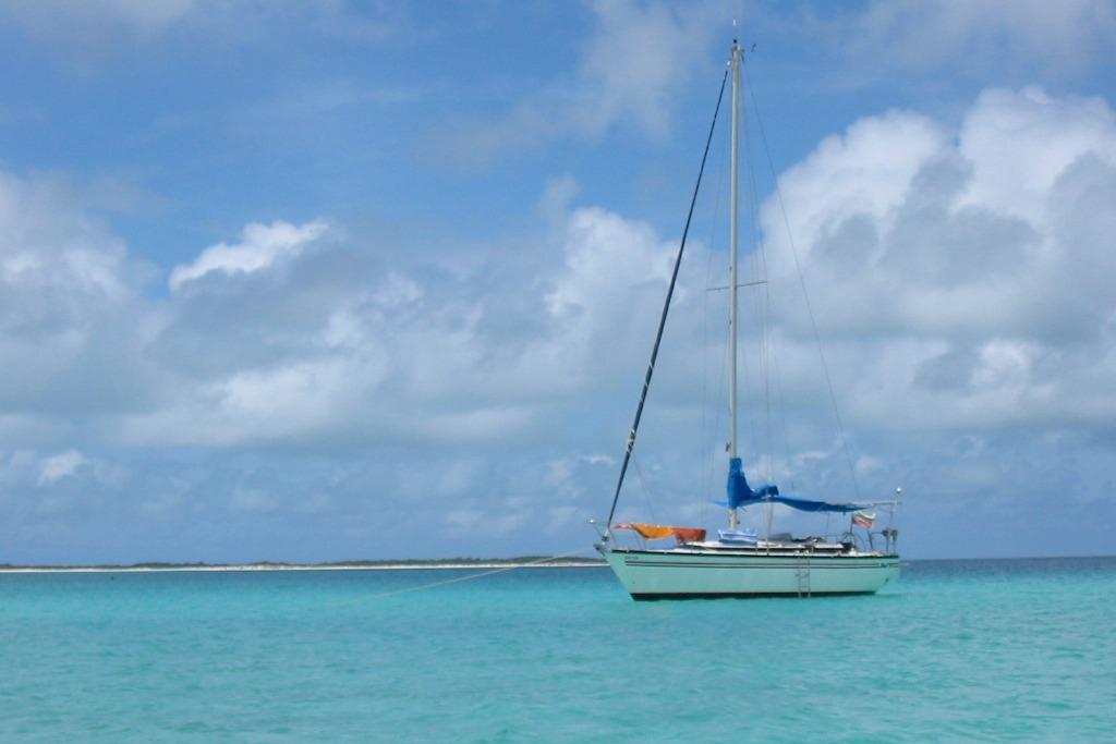 Sailboat Dufour 4800 (1982) anchored in turquoise waters under a cloudy sky.