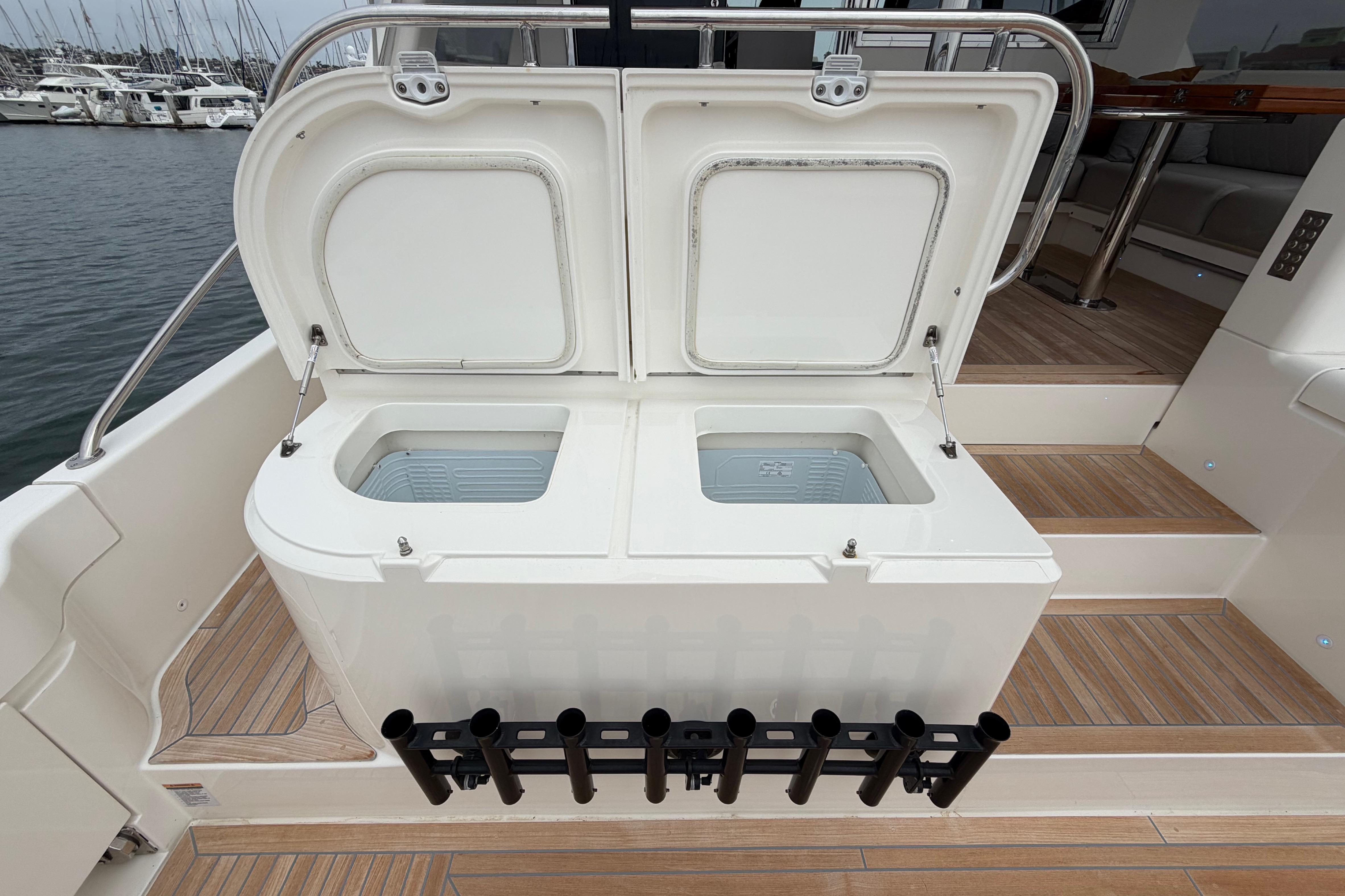 Open storage compartments on 2023 Riviera 645 SUV yacht deck, with rod holders and marina view.
