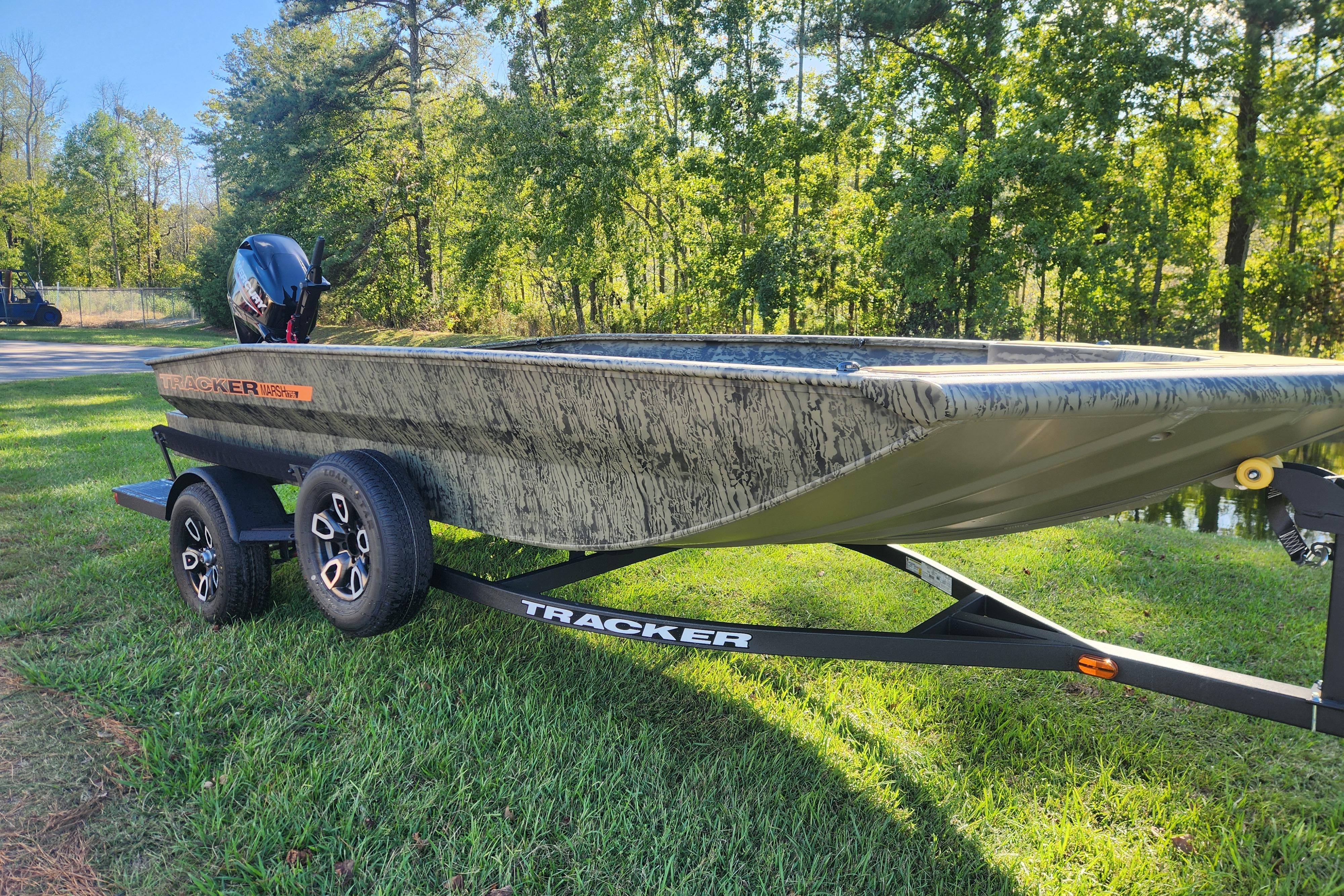 2026 Tracker Grizzly 1756 T Marsh boat on trailer, parked on grass with trees in background.