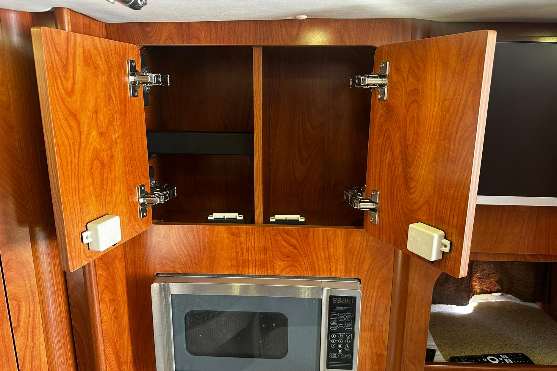Interior of 2012 Rinker 310 Express Cruiser LE with open wooden cabinets and microwave.