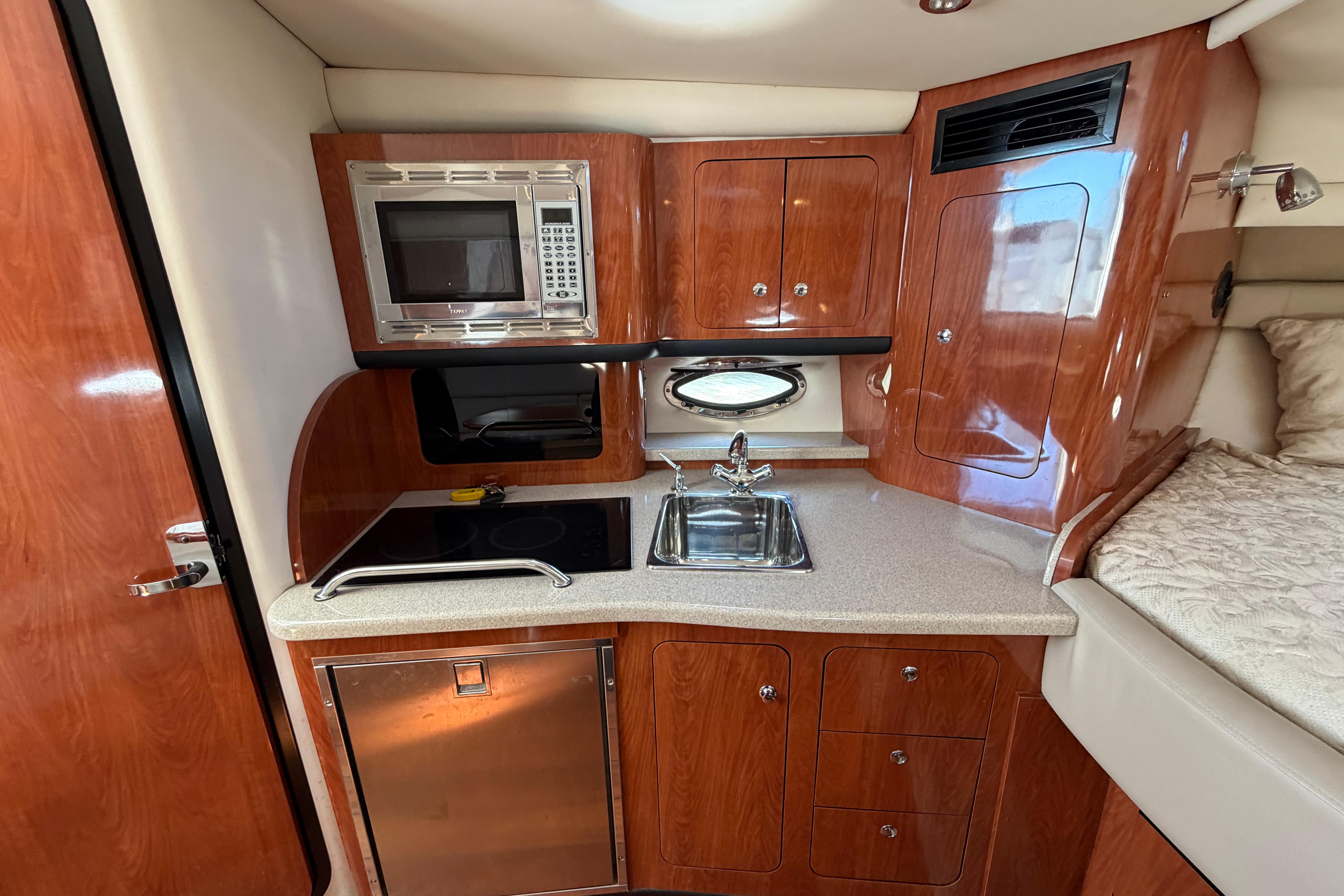 2008 Crownline 340 CR yacht interior with kitchenette, featuring microwave, sink, and wooden cabinetry.