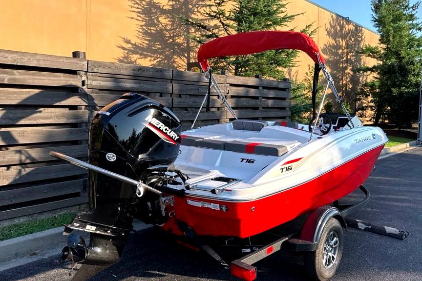 2026 Tahoe T16 boat with Mercury engine, red and white design, parked outdoors.