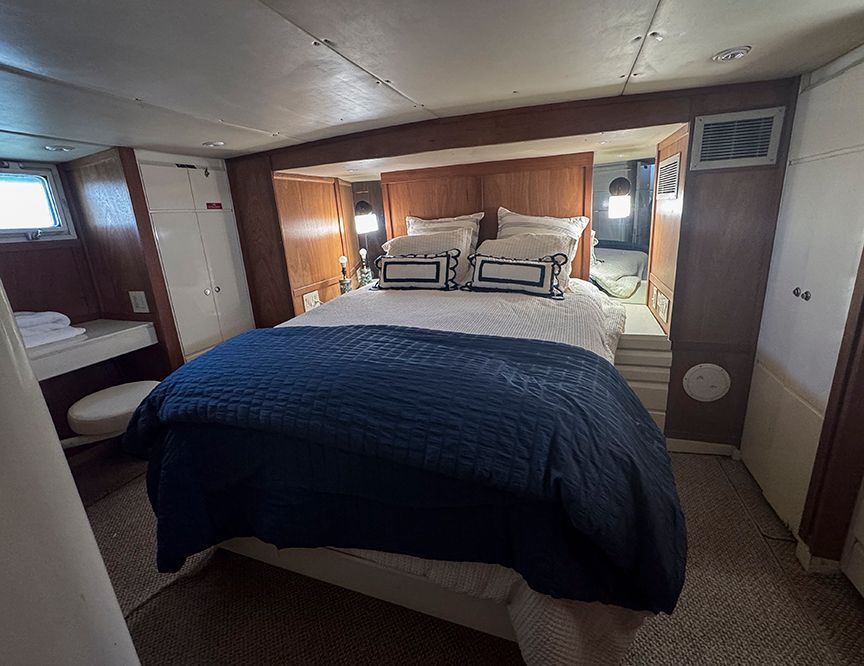 The image shows a cozy cabin with a large bed, wooden walls, and a small window.