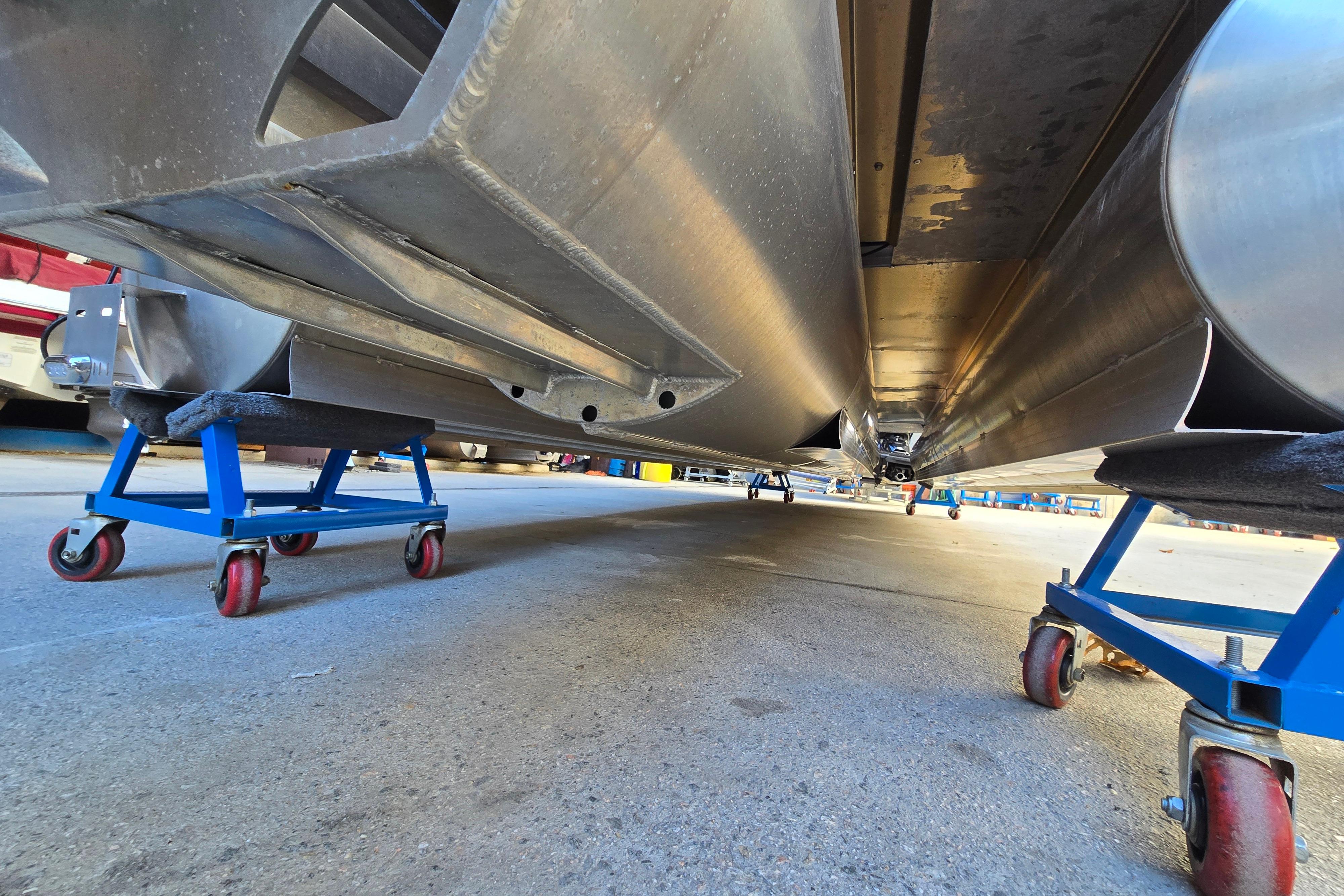 Underneath view of 2024 Godfrey Sweetwater 2486 SB pontoon boat on blue dollies.