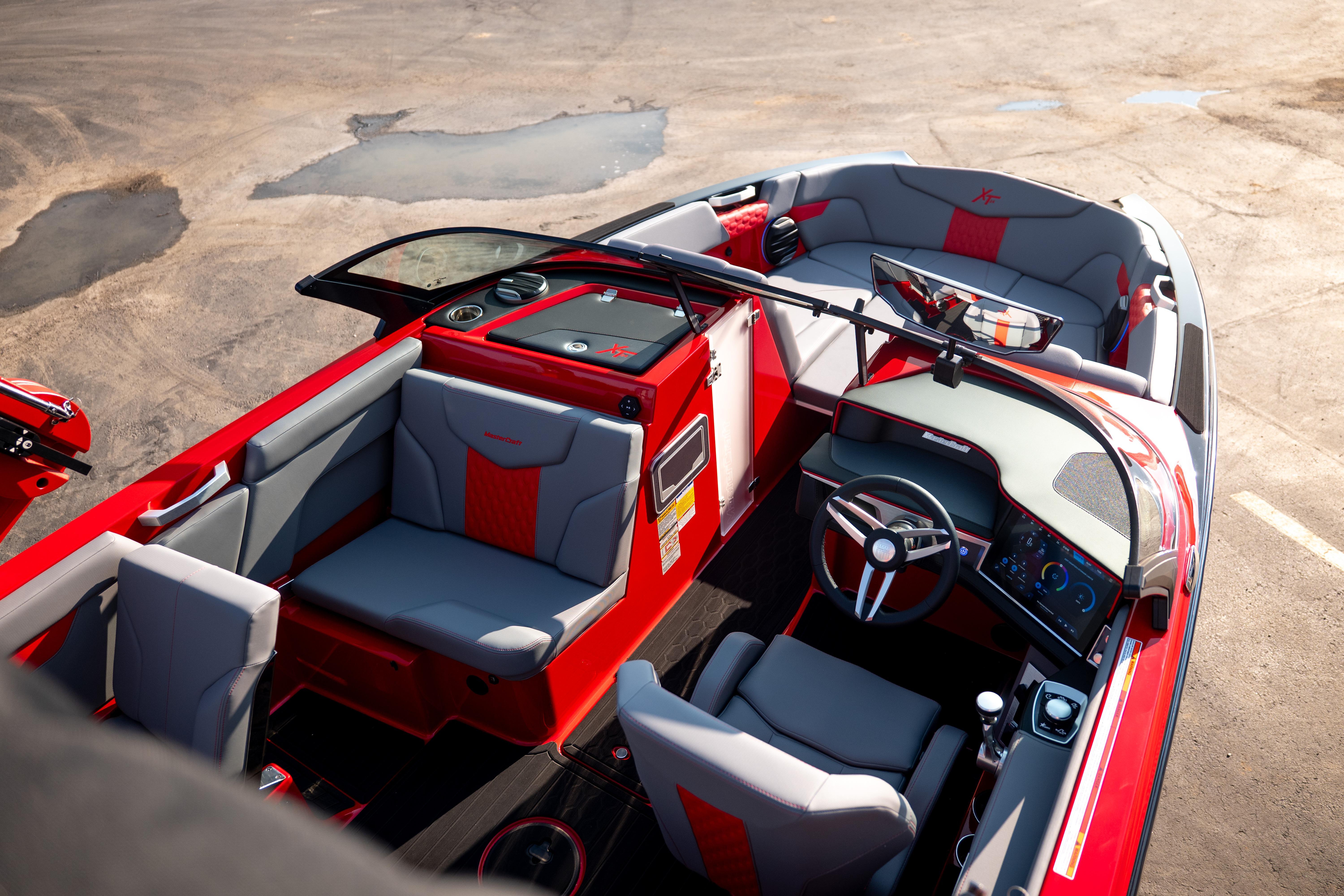 2027 MasterCraft XT24 boat interior with red and gray seating, modern dashboard, and steering wheel.