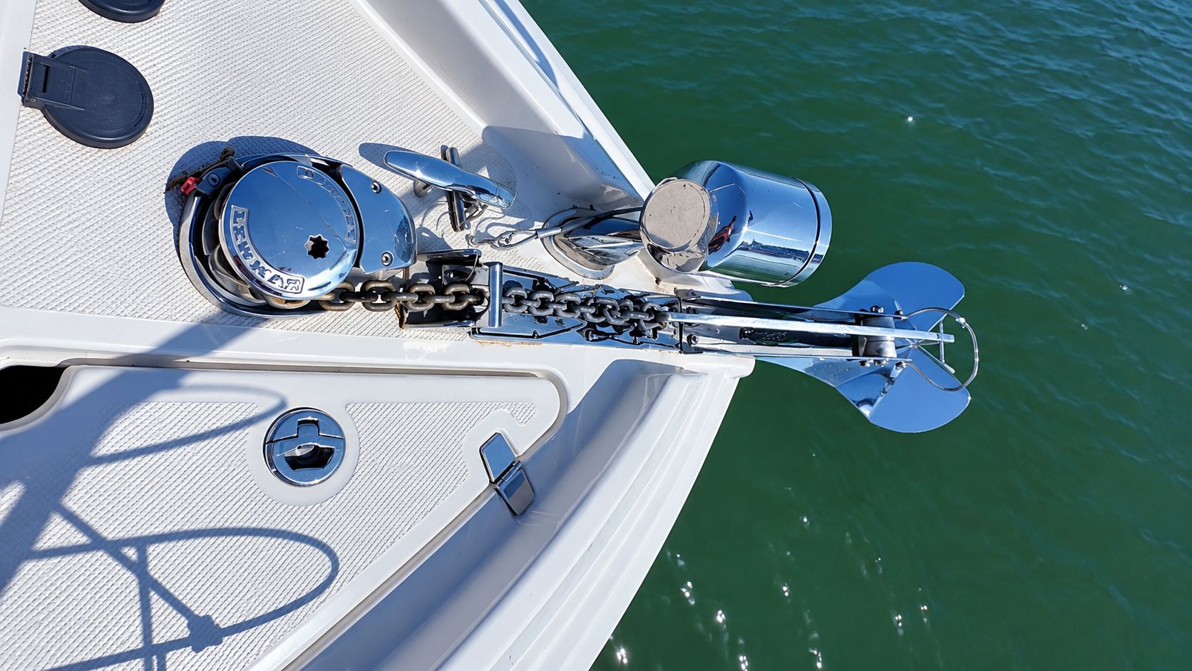 Bow of a boat with anchor and chain over green water.