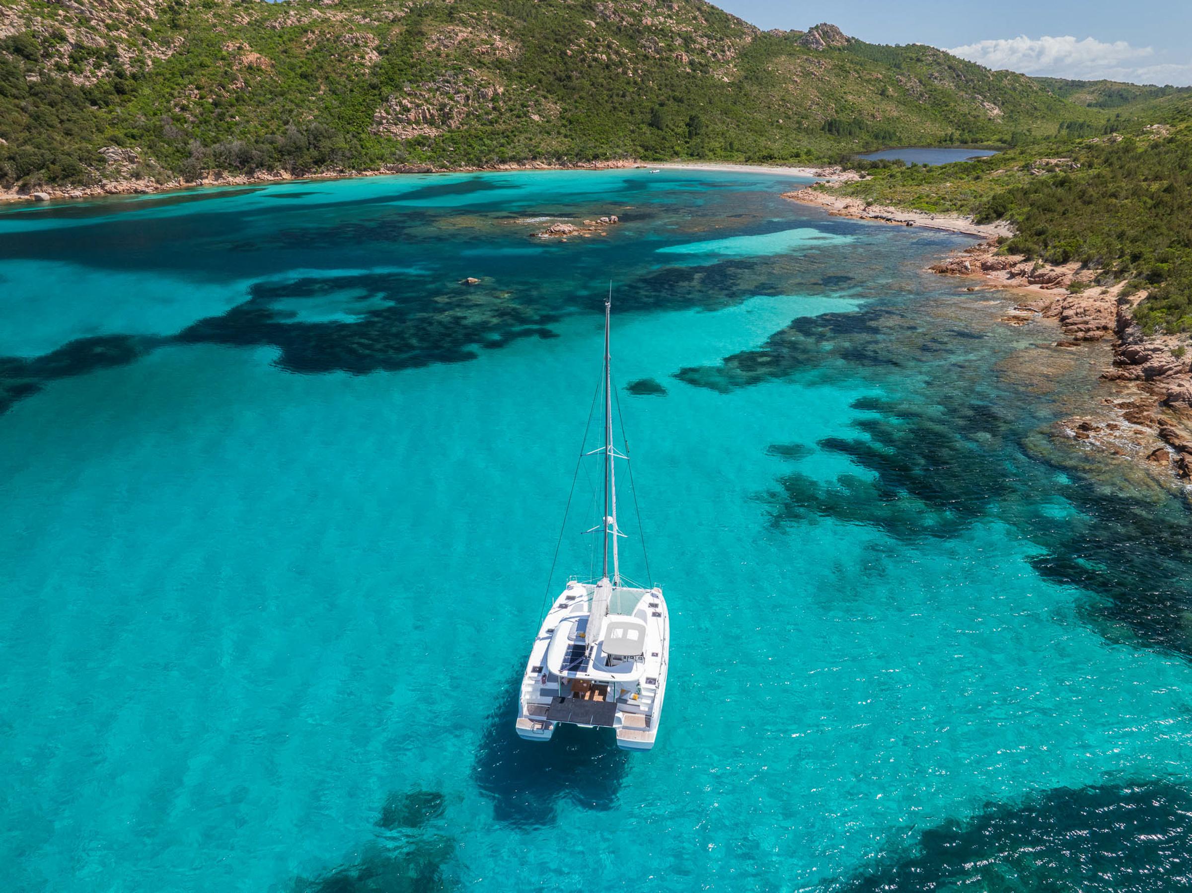 Aerial view of Lagoon 38 catamaran in turquoise waters, surrounded by lush green hills.