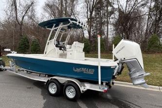 2026 Mako 24 APEX boat on trailer, blue hull, white motor, parked outdoors.