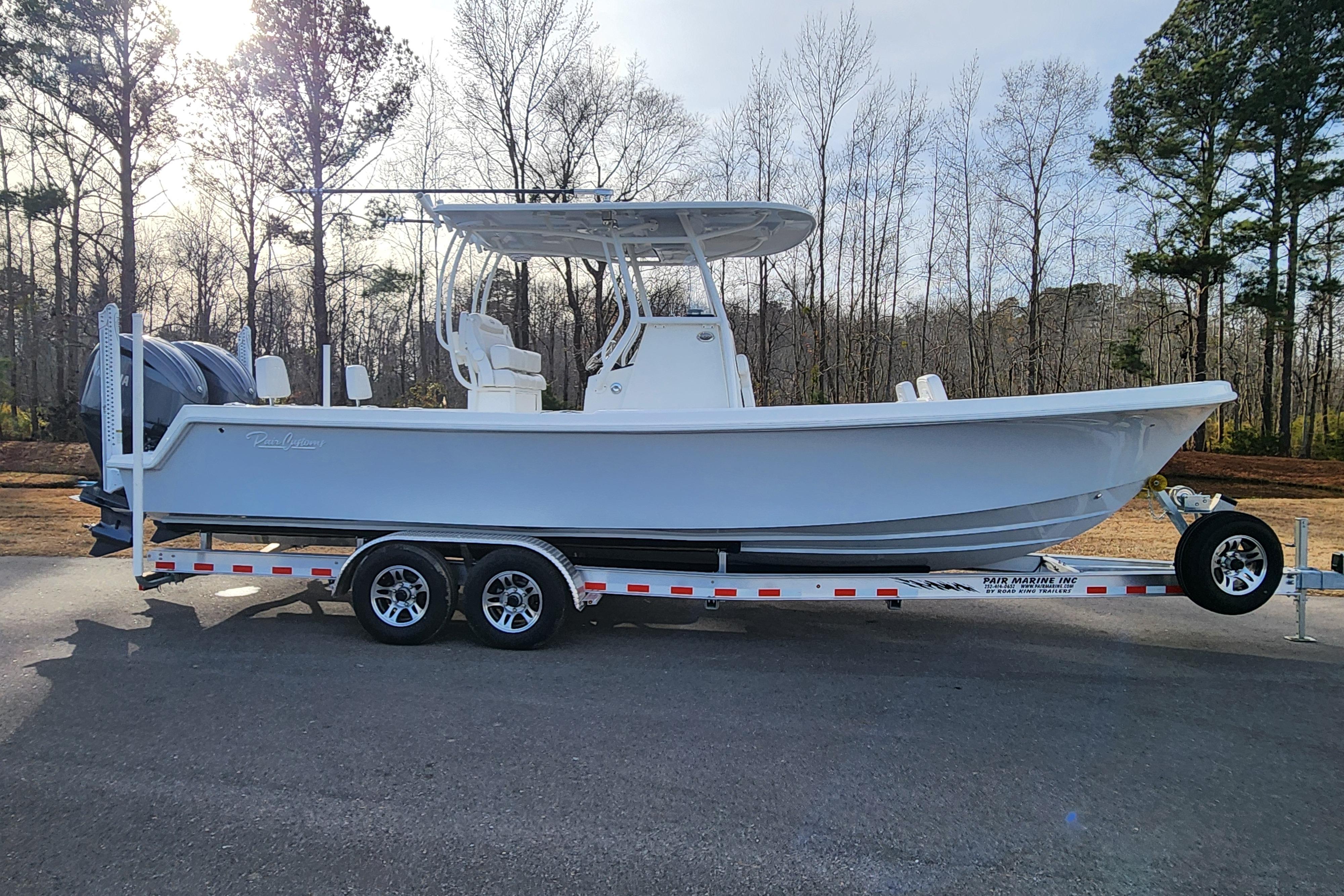 2024 Pair Customs 27 CC boat on trailer, parked outdoors, surrounded by trees.