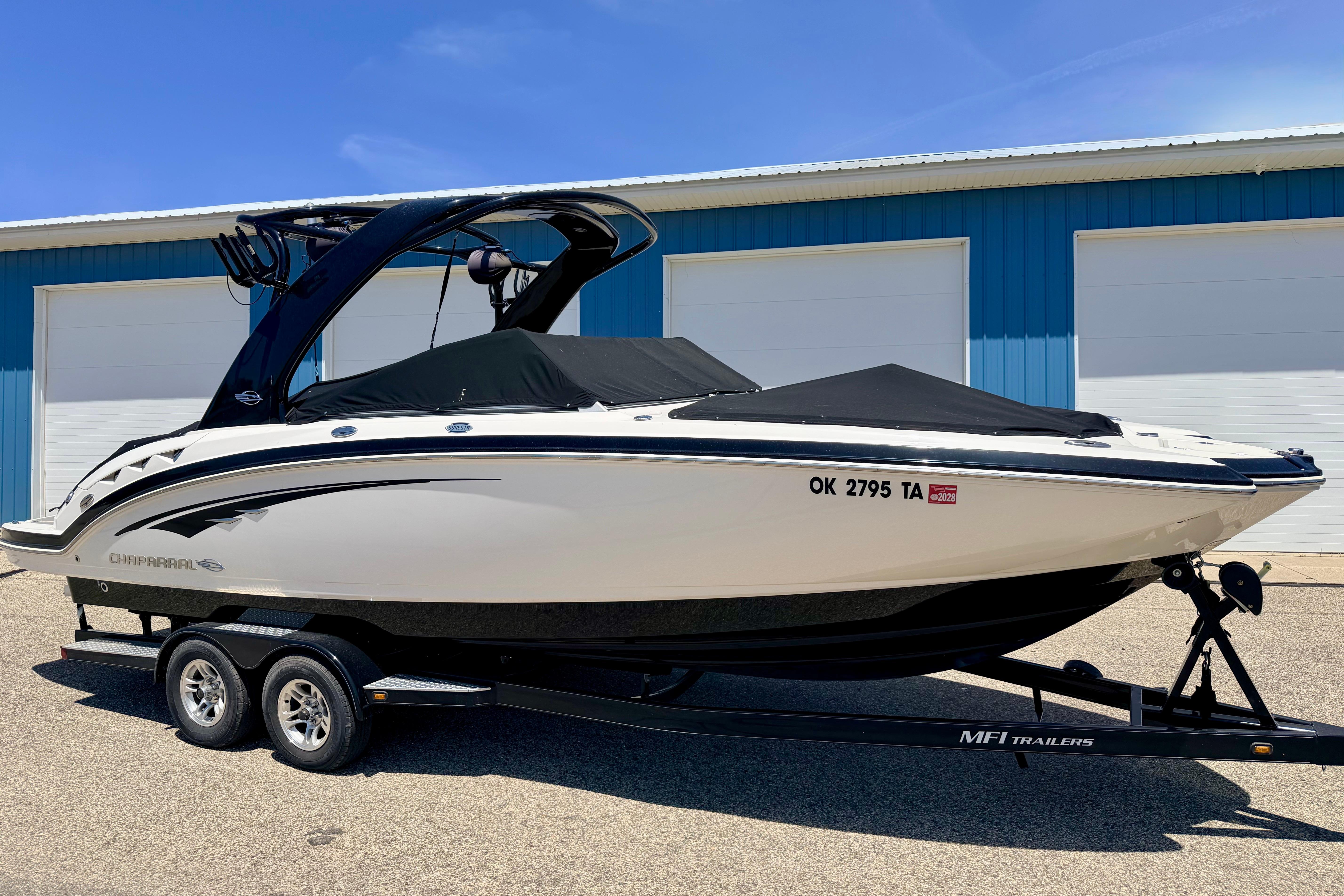 2015 Chaparral Sunesta 264 boat on trailer, parked outside blue building.