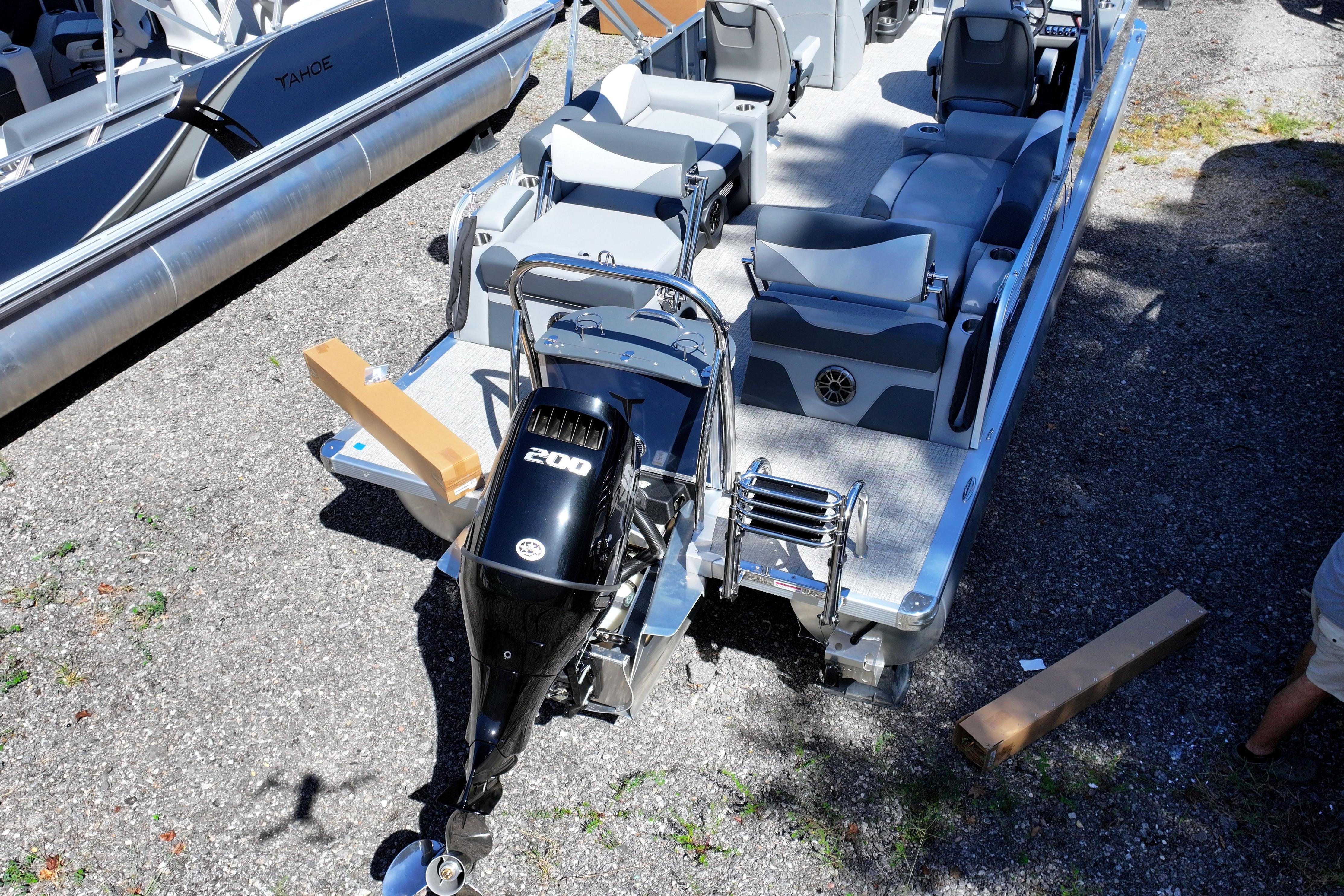2026 Tahoe Pontoon LTZ Quad Lounger with powerful outboard motor, parked on gravel.