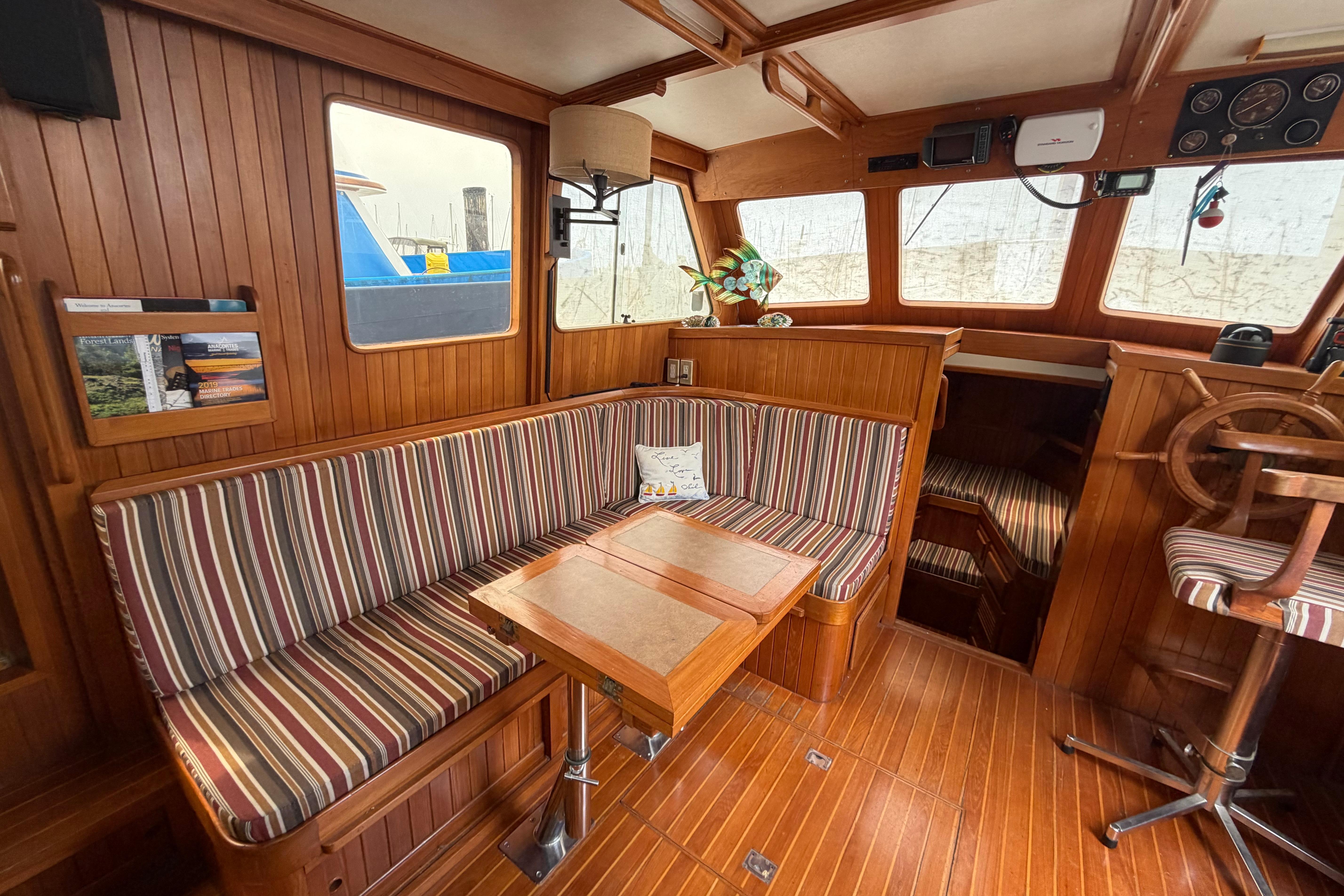 Cozy 1988 Monk 36 boat interior with striped seating, wooden accents, and helm station.
