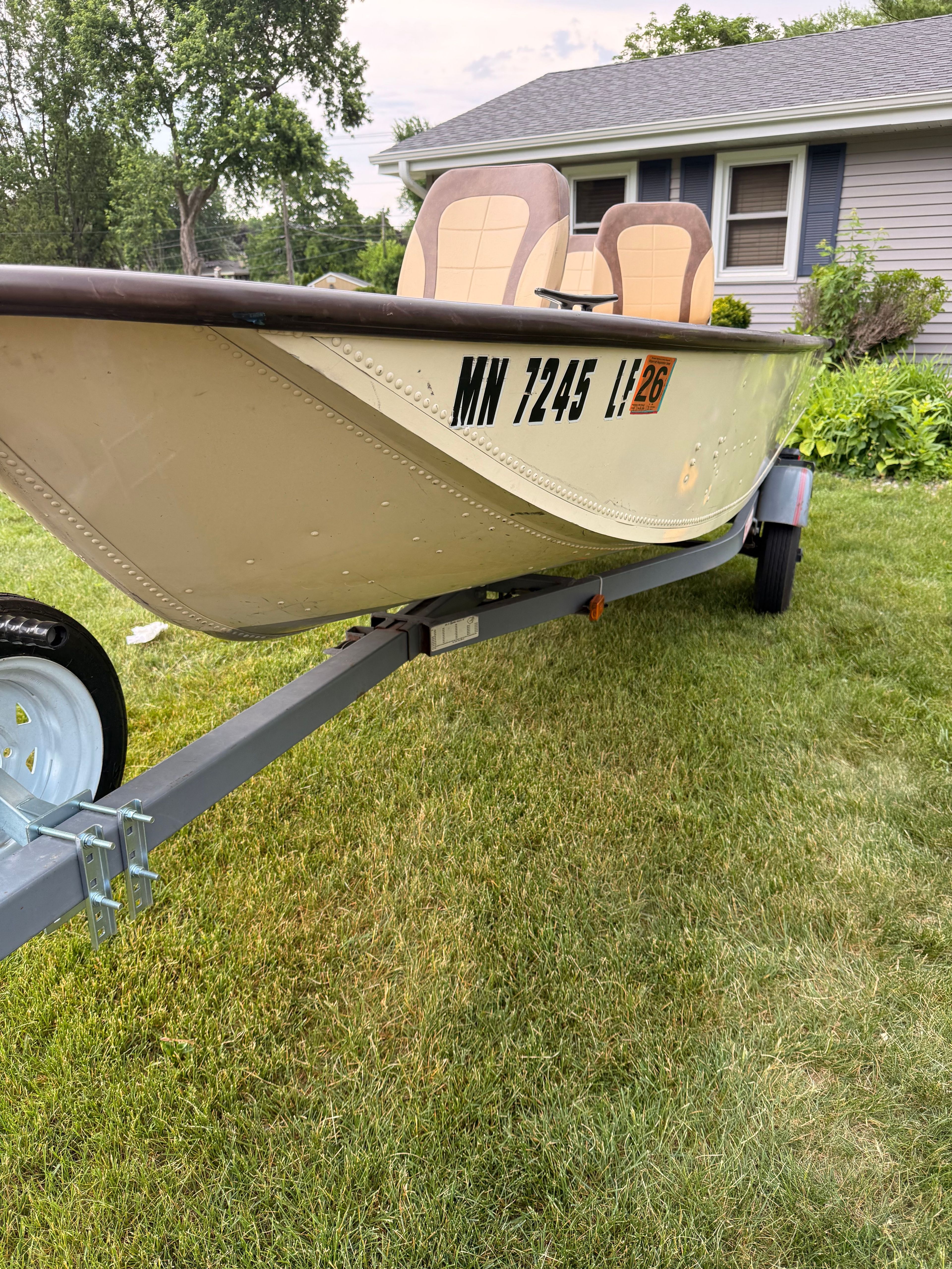 A 1985 Grumman 4.4 boat on a trailer in a yard.