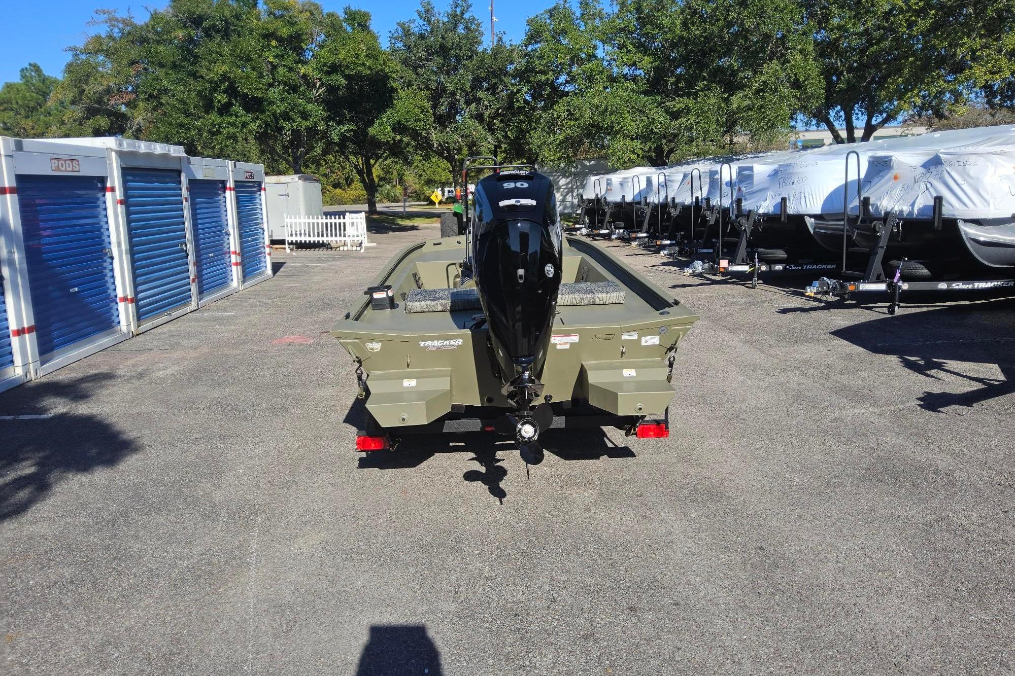 2026 Tracker Grizzly 1860 CC boat with motor, parked outdoors near storage units.