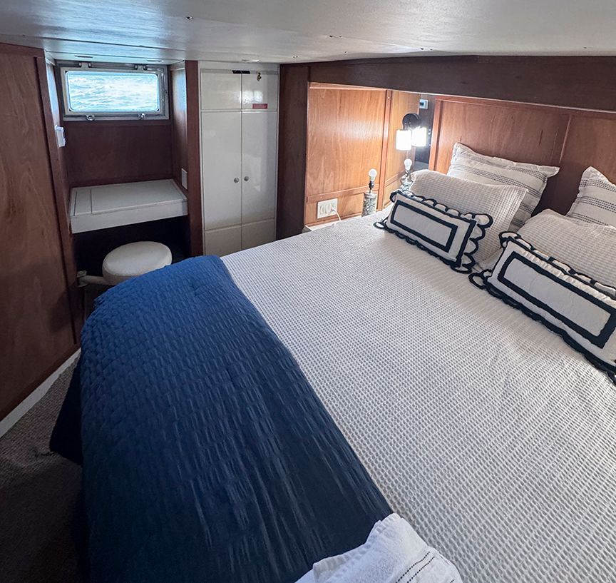 Cabin with double bed, blue and white pillows, wood paneling, and a small window.