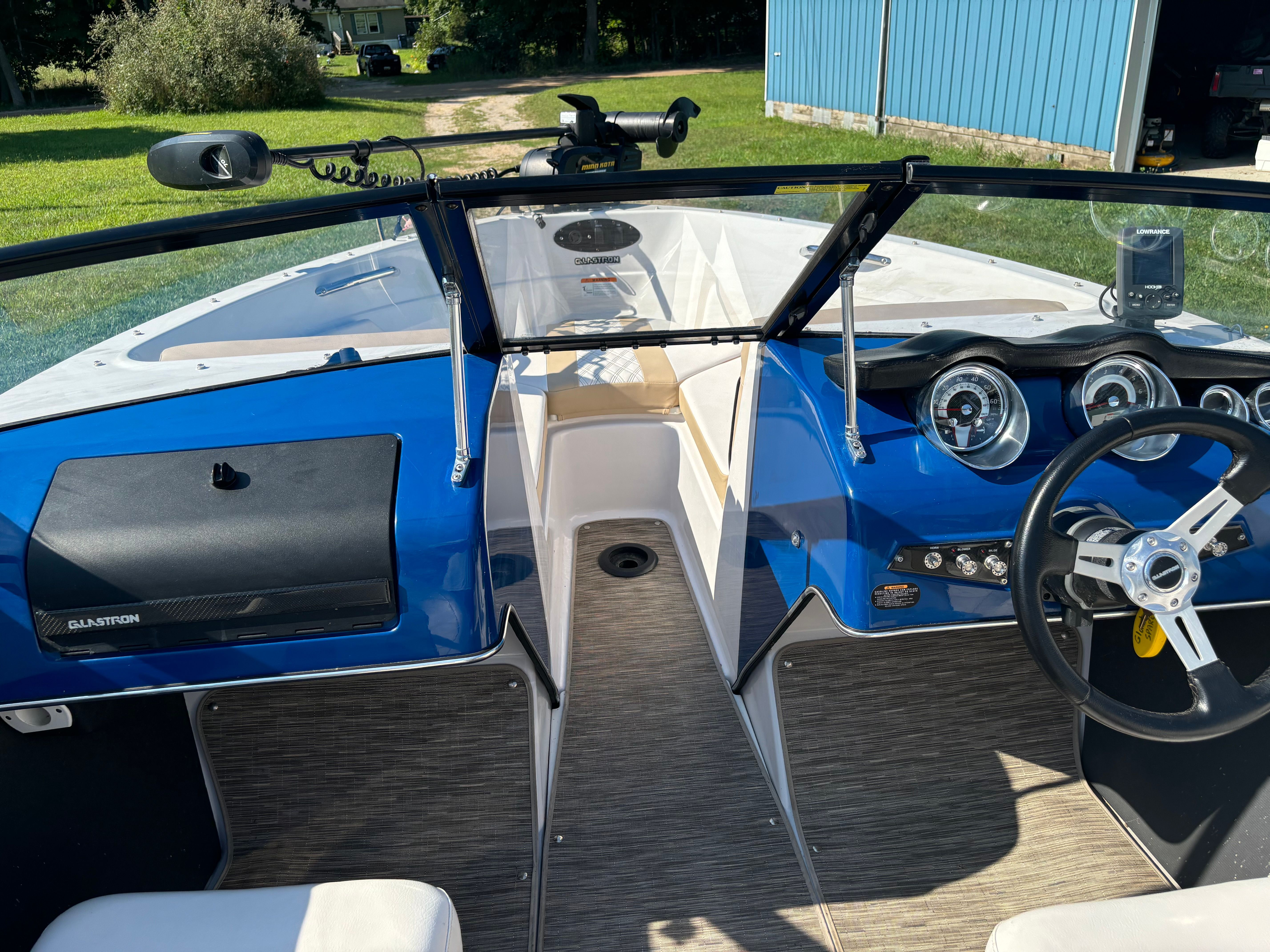 The cockpit of a Glastron GTSF 185 boat with a blue dashboard and steering wheel.