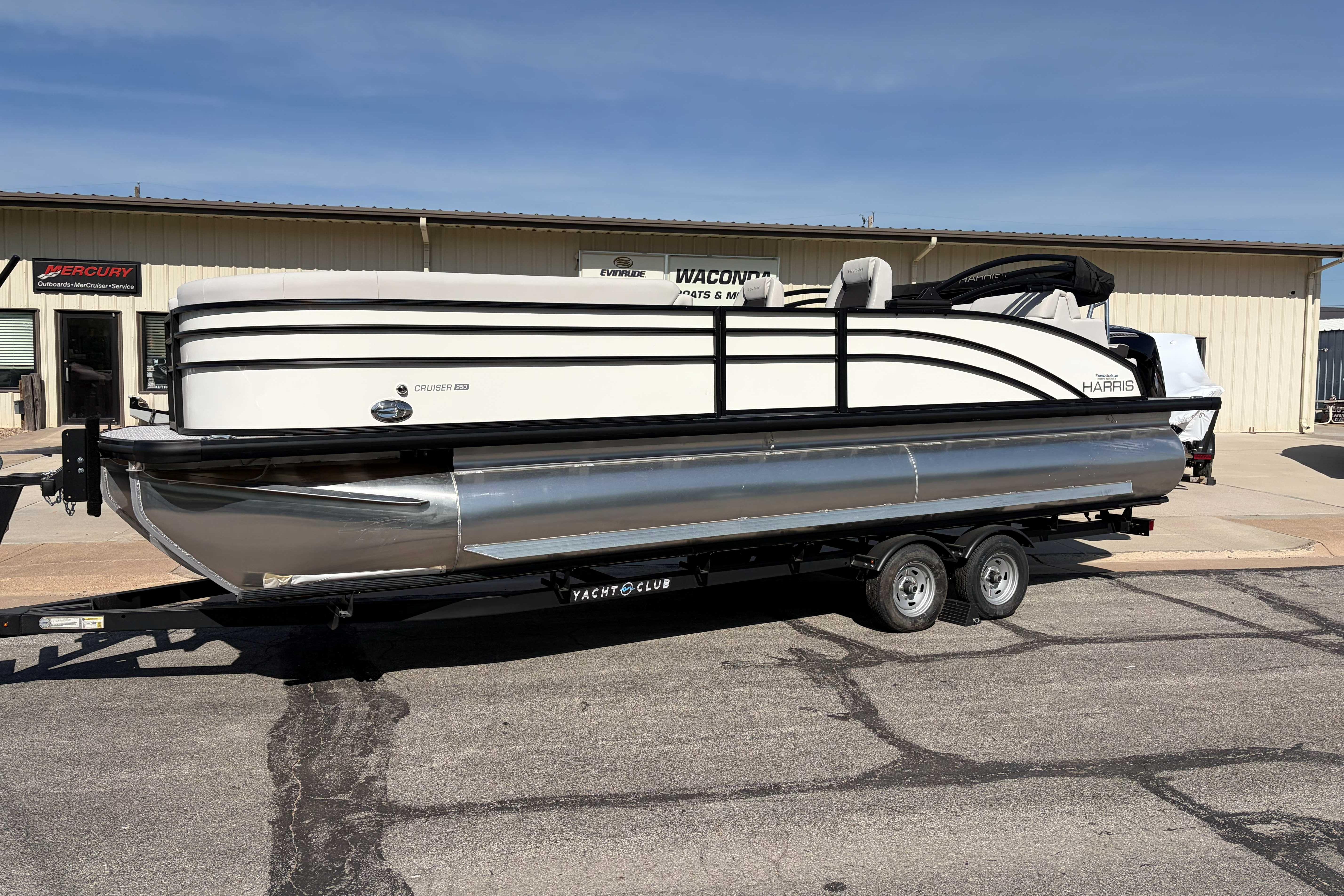 2025 Harris Cruiser 250 pontoon boat on trailer, parked outside dealership.