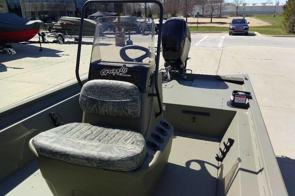 2026 Tracker Grizzly 1860 CC boat with camouflage seating and steering console, parked outdoors.