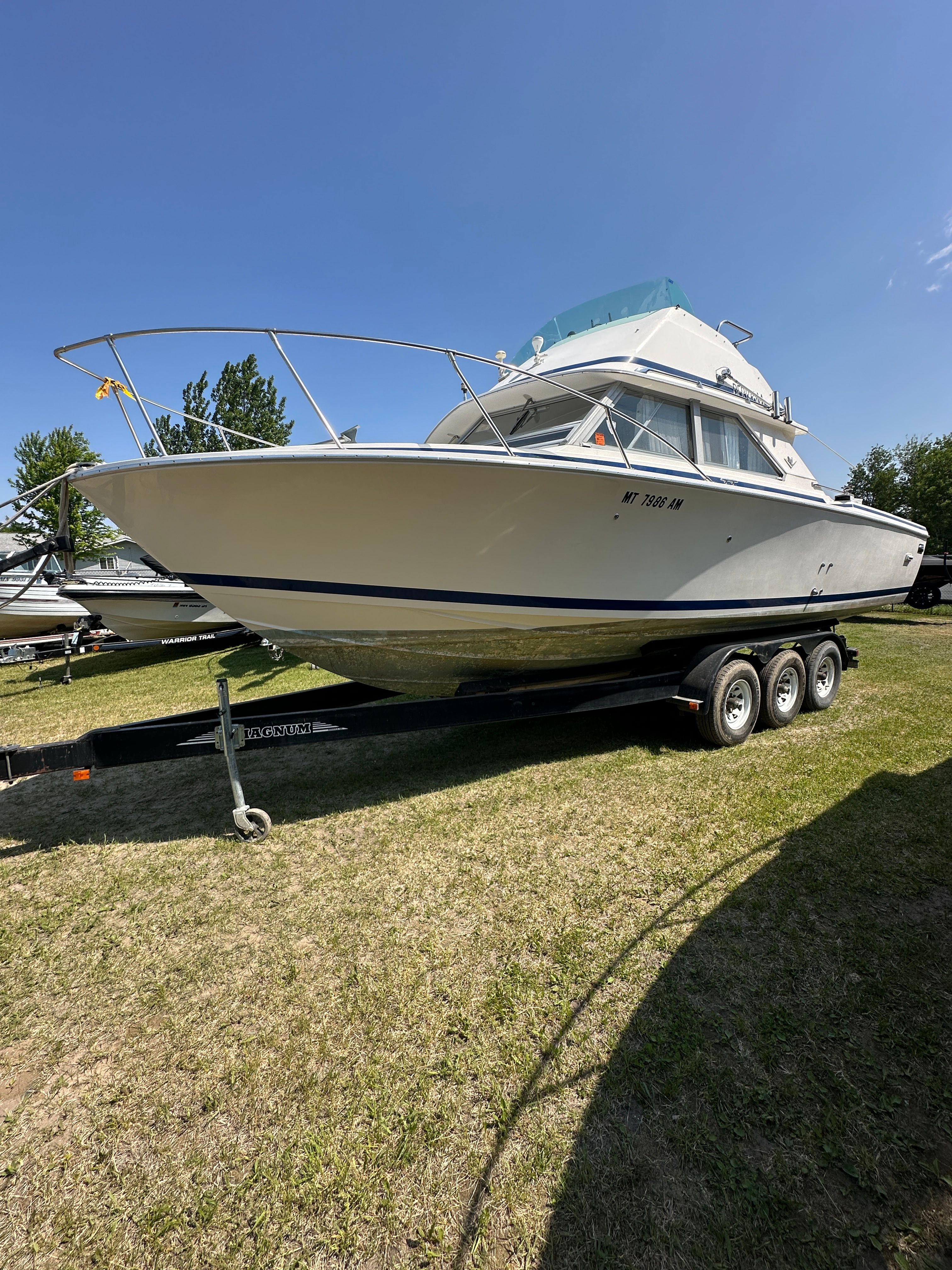 A 1983 Bertram Flybridge Cruiser is on a trailer on a grassy area.
