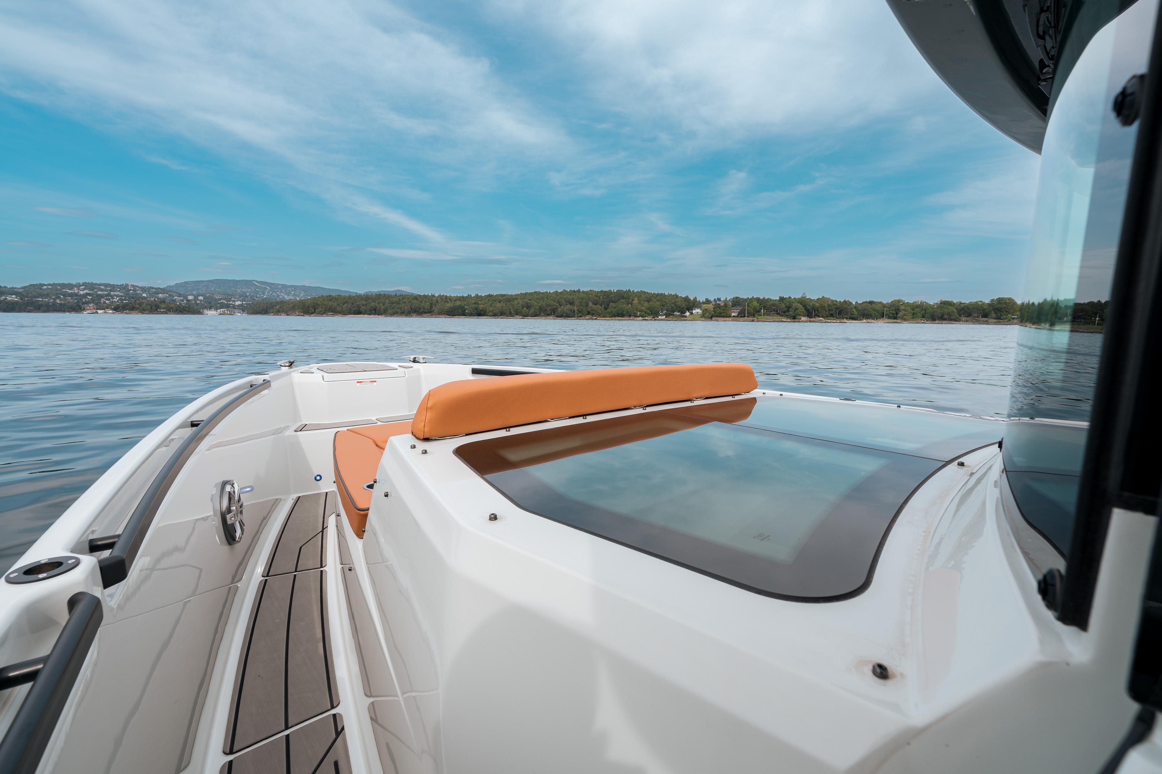 2023 Saxdor 320 GTC boat cruising on a serene lake under a clear blue sky.