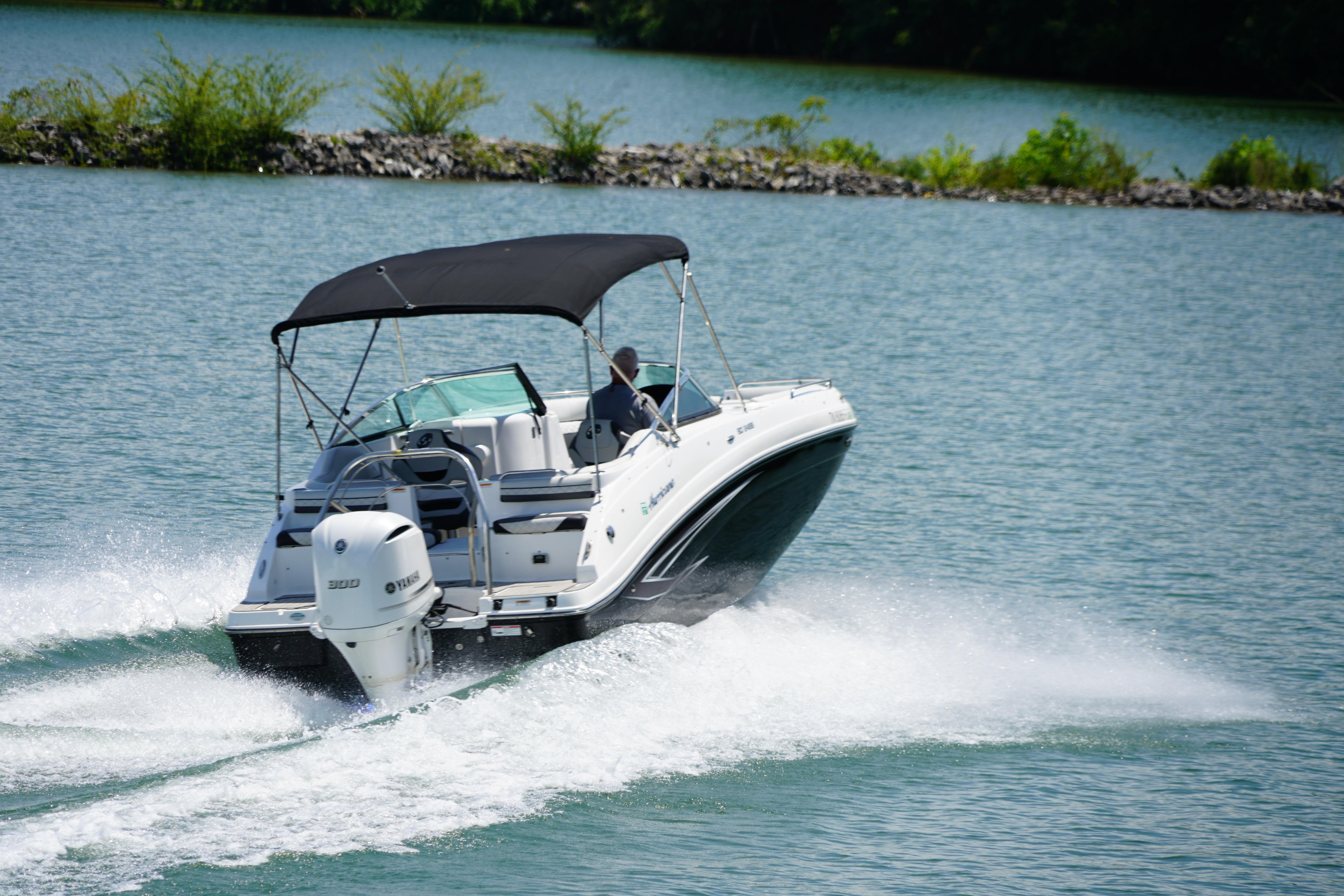 2020 Hurricane SunDeck 2486 OB cruising on a serene lake with lush greenery.