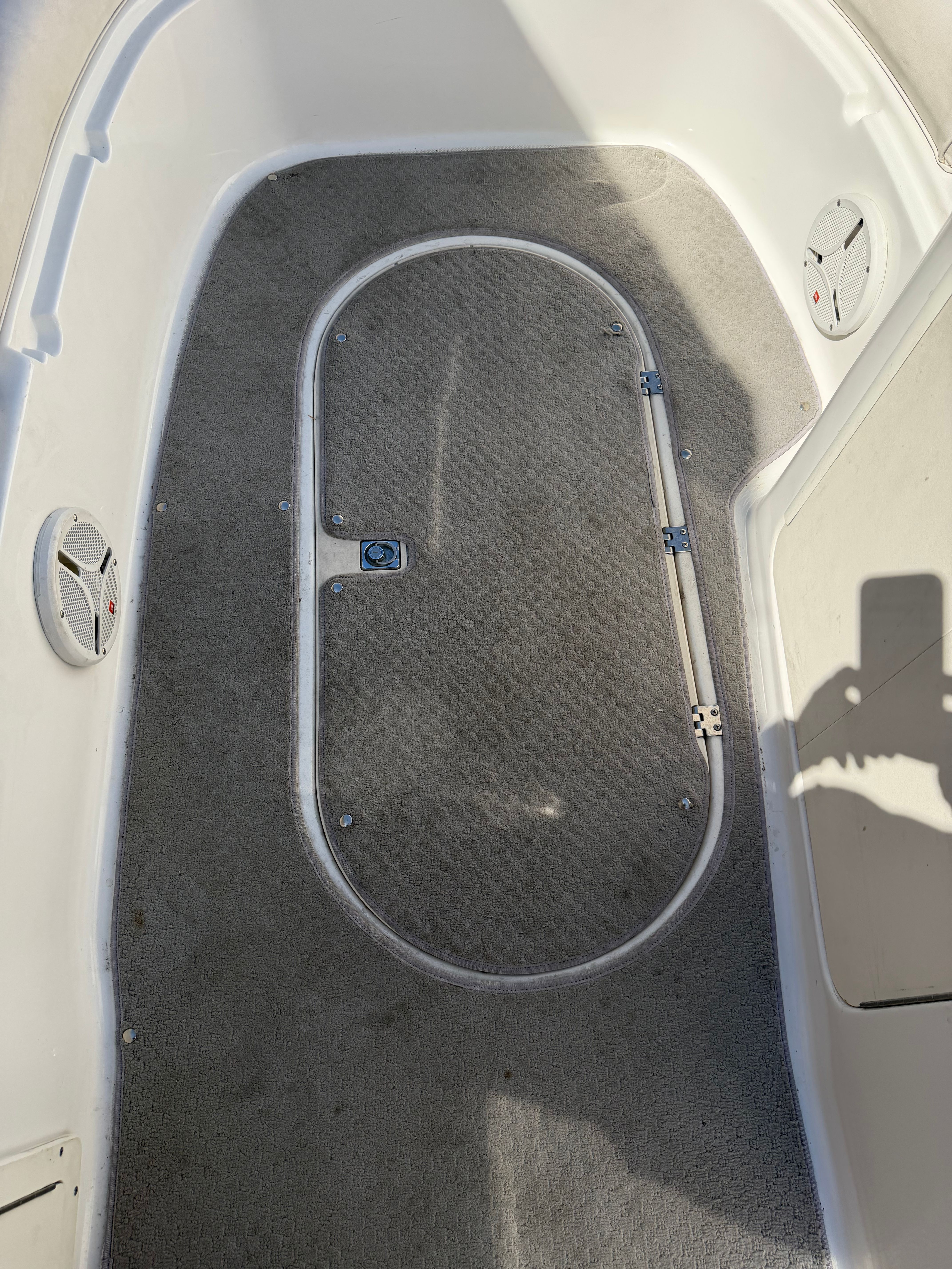 Interior of a boat with gray carpet flooring and an oval access panel.