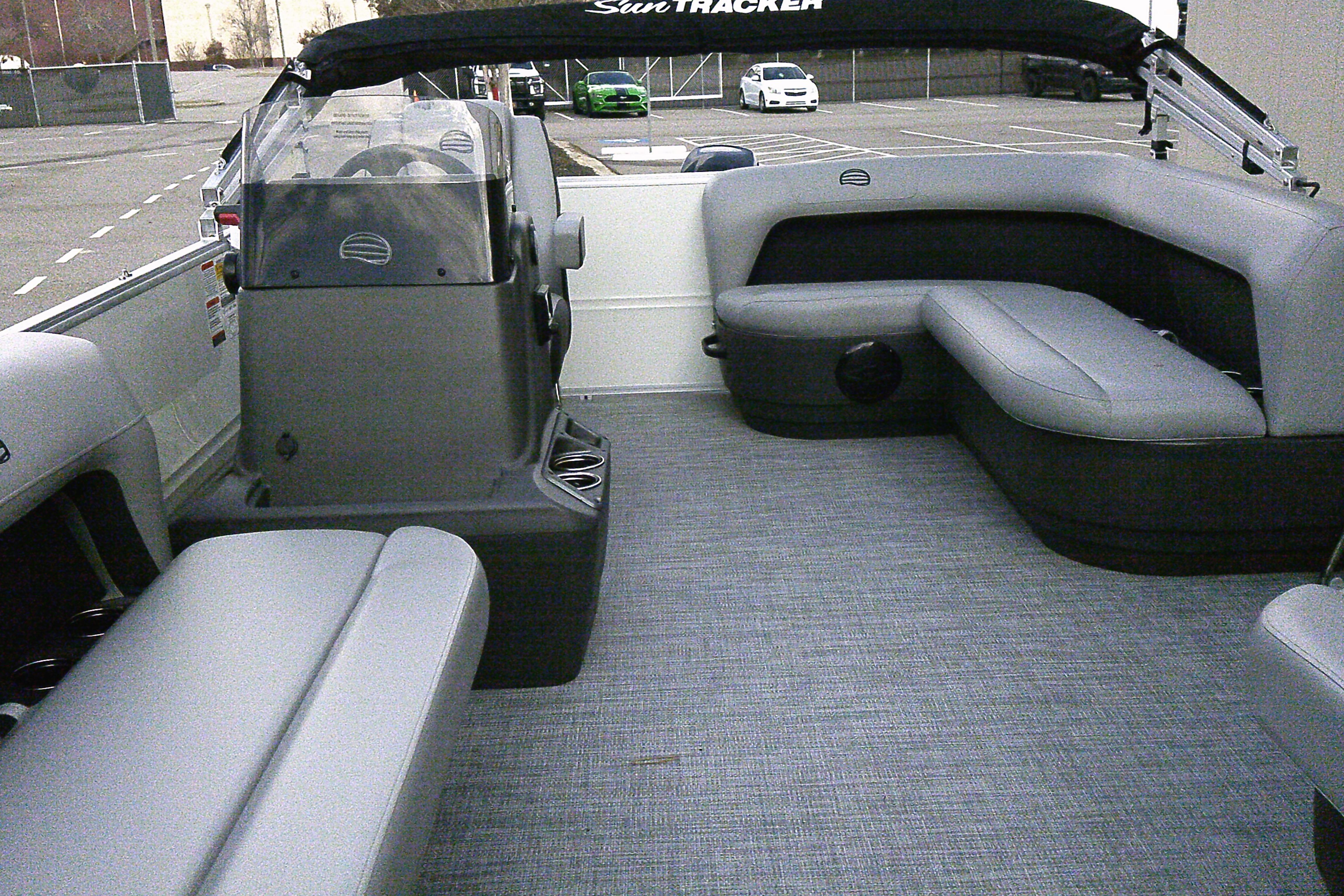 2026 Sun Tracker Party Barge 16 DLX interior with gray seating and helm in a parking lot.