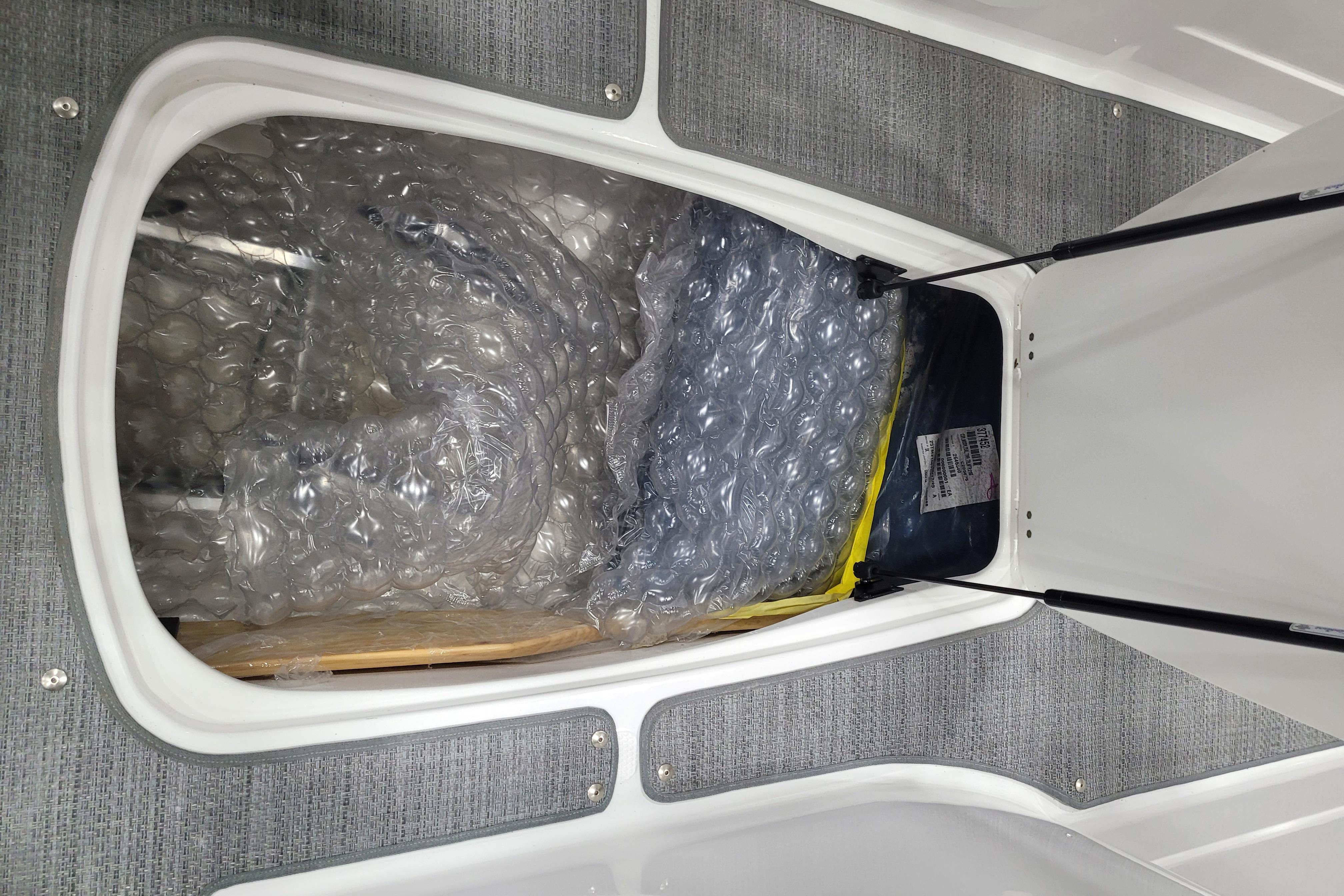 Storage compartment in 2026 Tahoe 2150 boat, featuring bubble-wrapped items and carpeted interior.