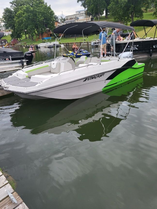 A 2023 Starcraft SVX 191 OB boat docked. It features green accents and a sunshade.